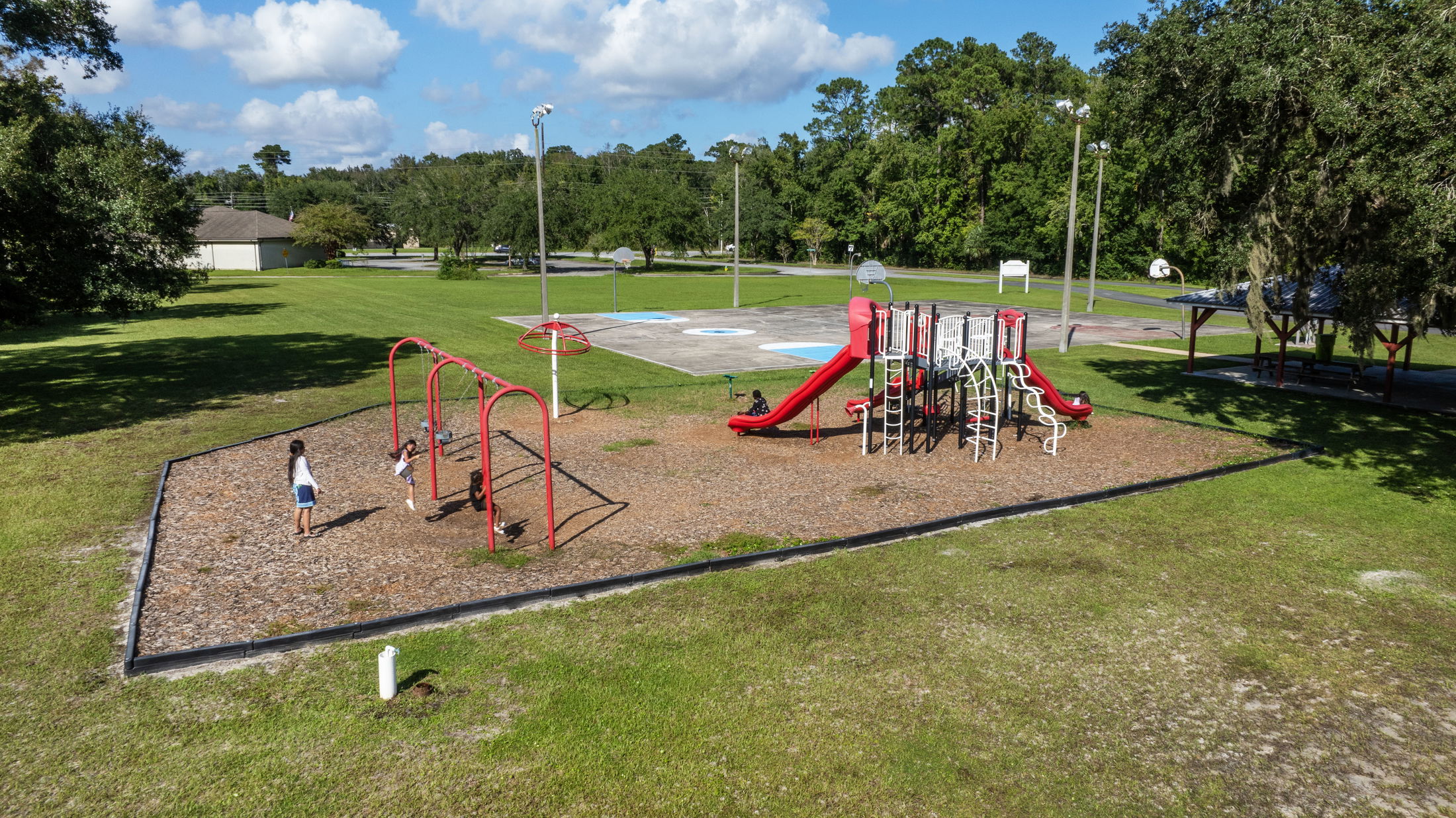 Aerial view of a vibrant playground with swings and slides, surrounded by lush greenery and clear blue skies, capturing children playing outdoors.