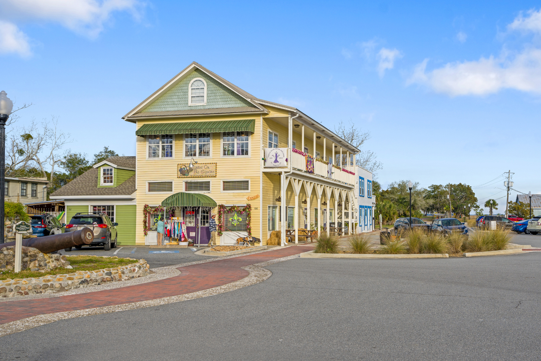 Charming two-story yellow and green building with a store and balcony, set in a quaint small-town square on a sunny day.