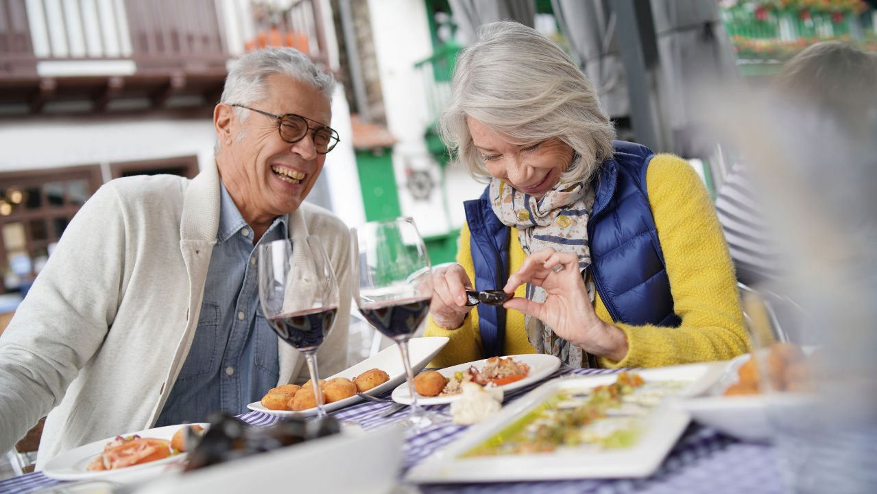 Smiling older couple enjoying wine and food at an outdoor restaurant.