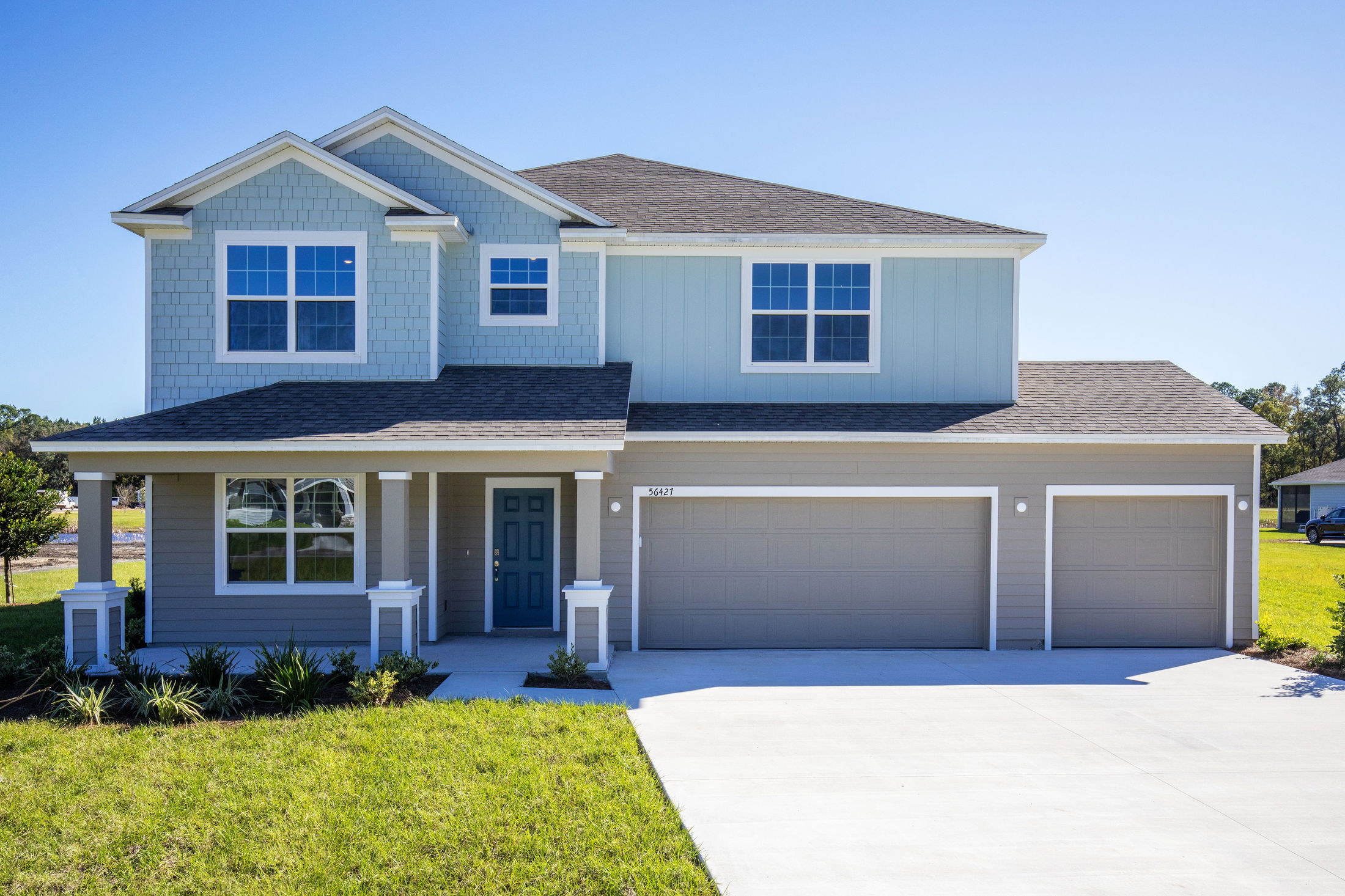 Front view of a modern two-story family home with a blue exterior, landscaped yard, and double garage.