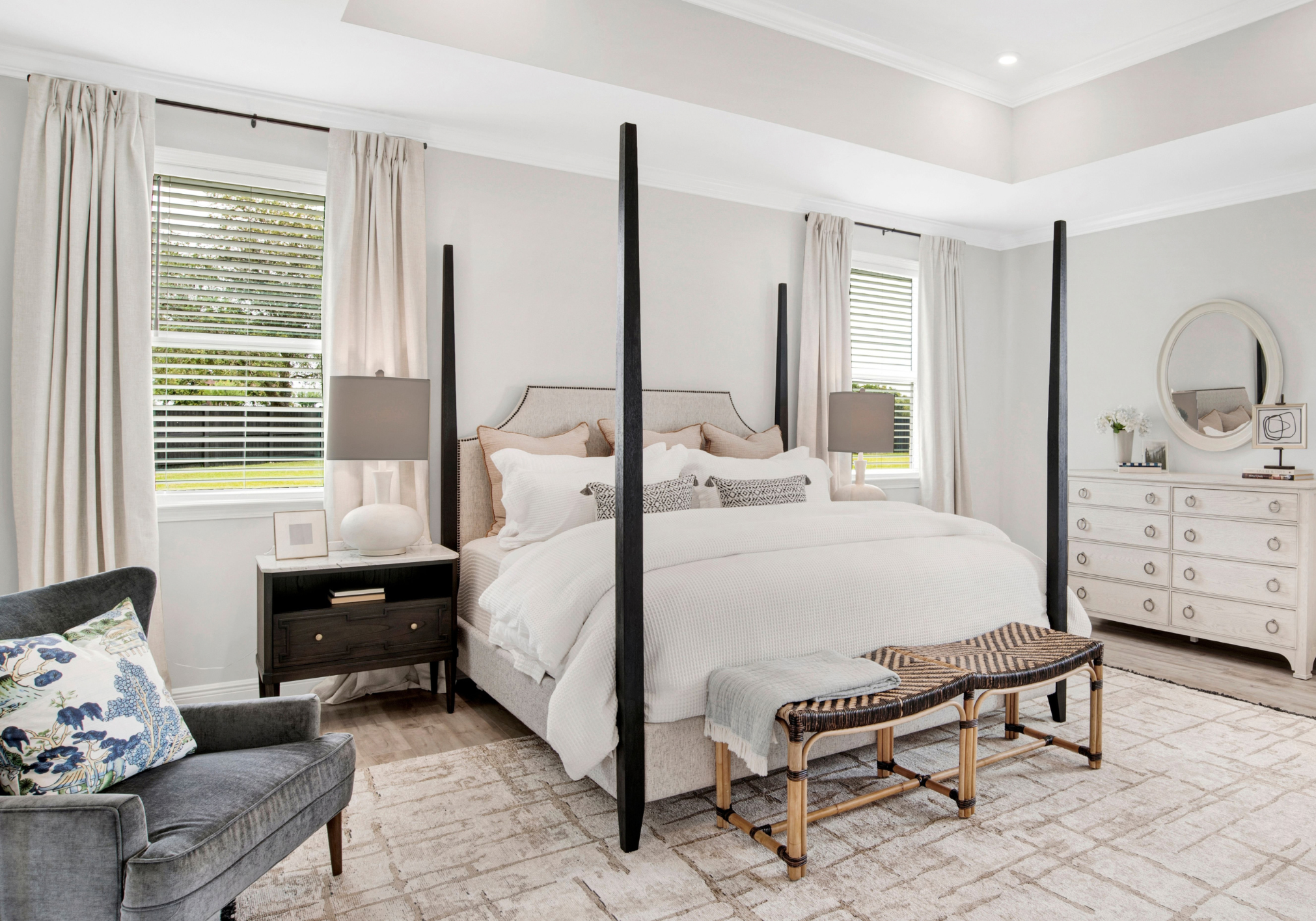 A modern bedroom featuring a four-poster bed, two lamps on nightstands, a decorative mirror, and a comfortable armchair.