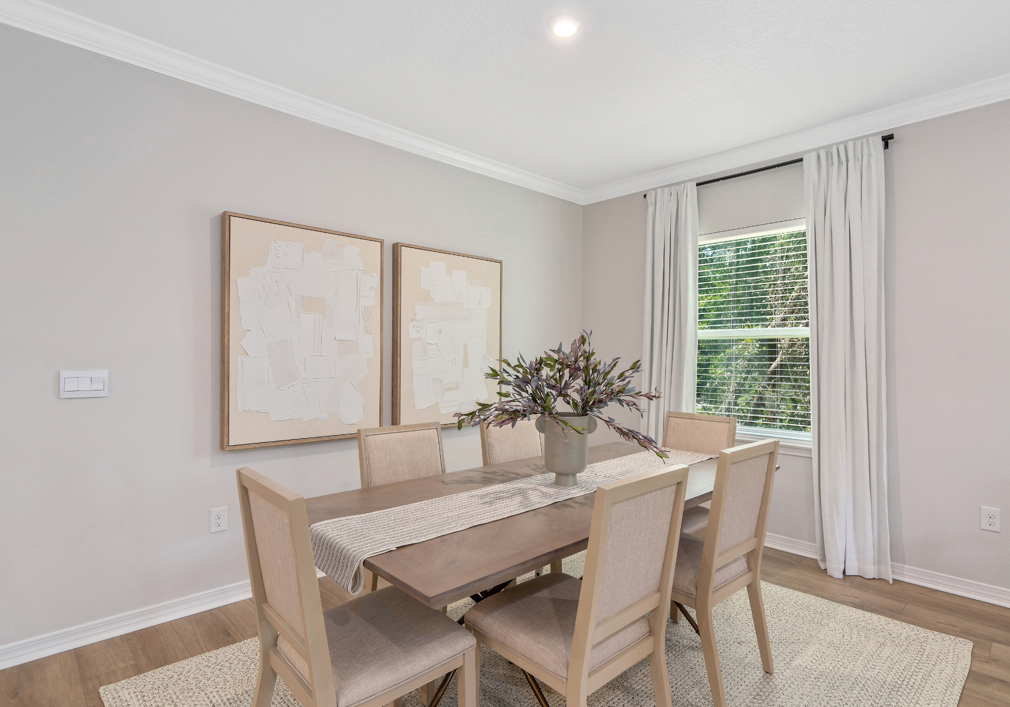 A dining room with a wooden table, six chairs, a vase of flowers, and two abstract wall art pieces.