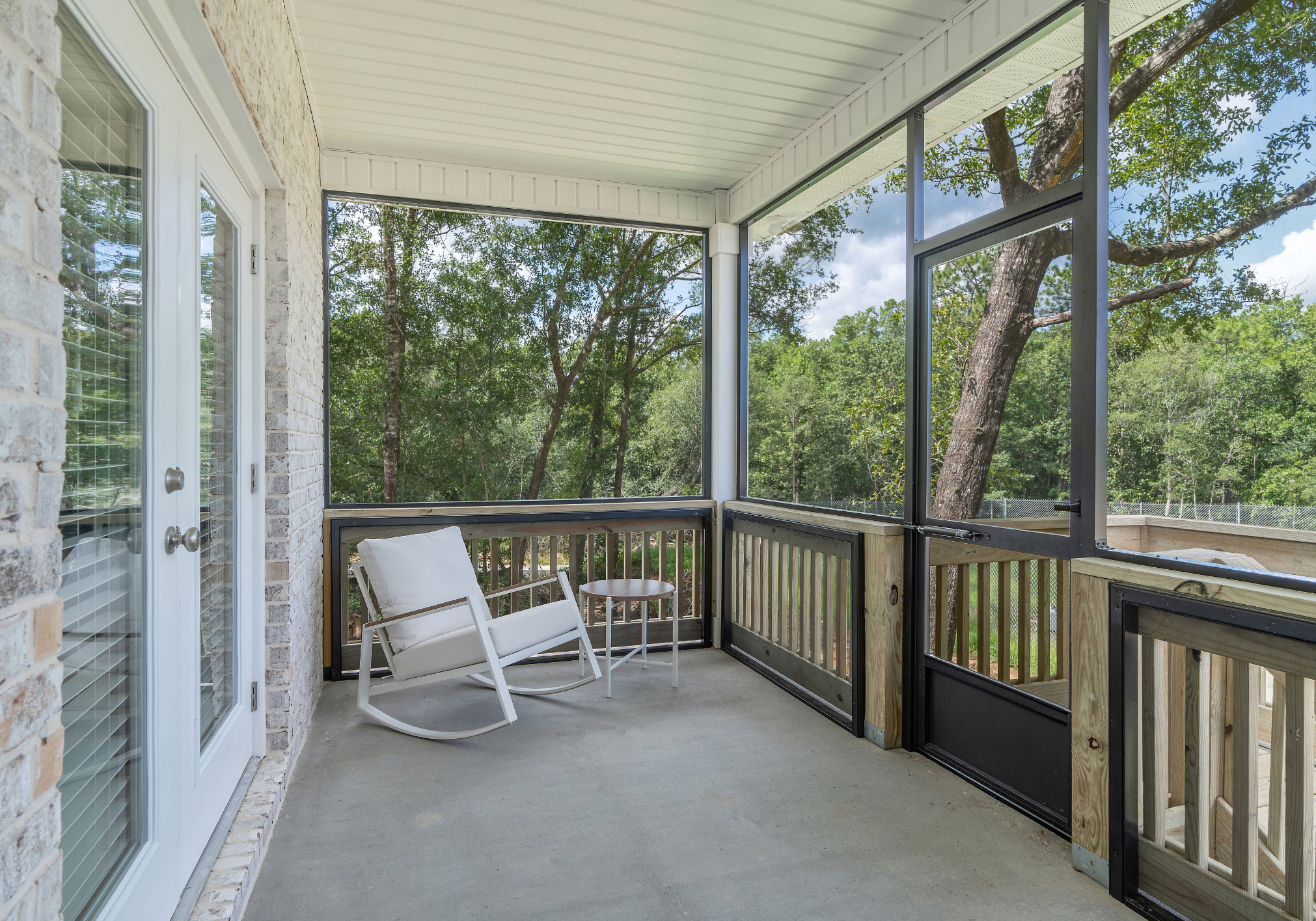 A screened-in porch featuring a rocking chair and a small table, surrounded by trees.