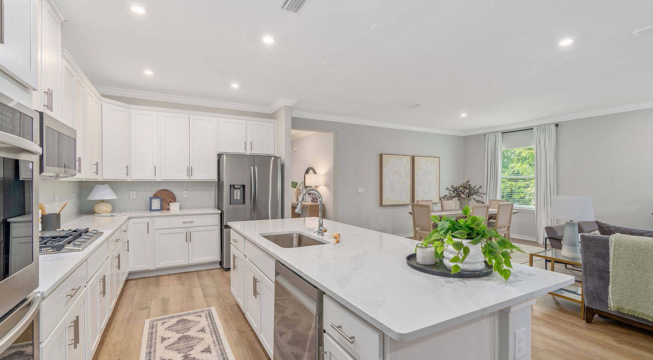 Modern open-concept kitchen and dining area with white cabinets, stainless steel appliances, and a light wood floor.