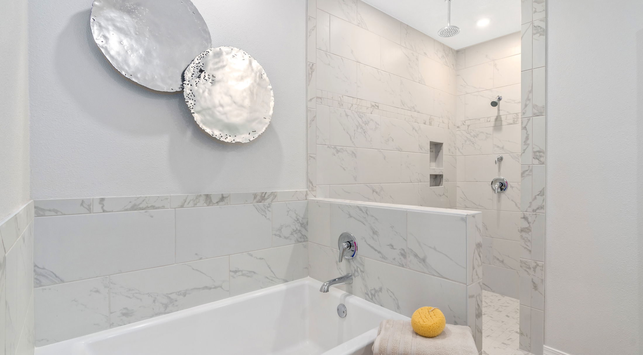 Modern bathroom with marble tiles, a spacious walk-in shower, and elegant wall art featuring metallic discs.