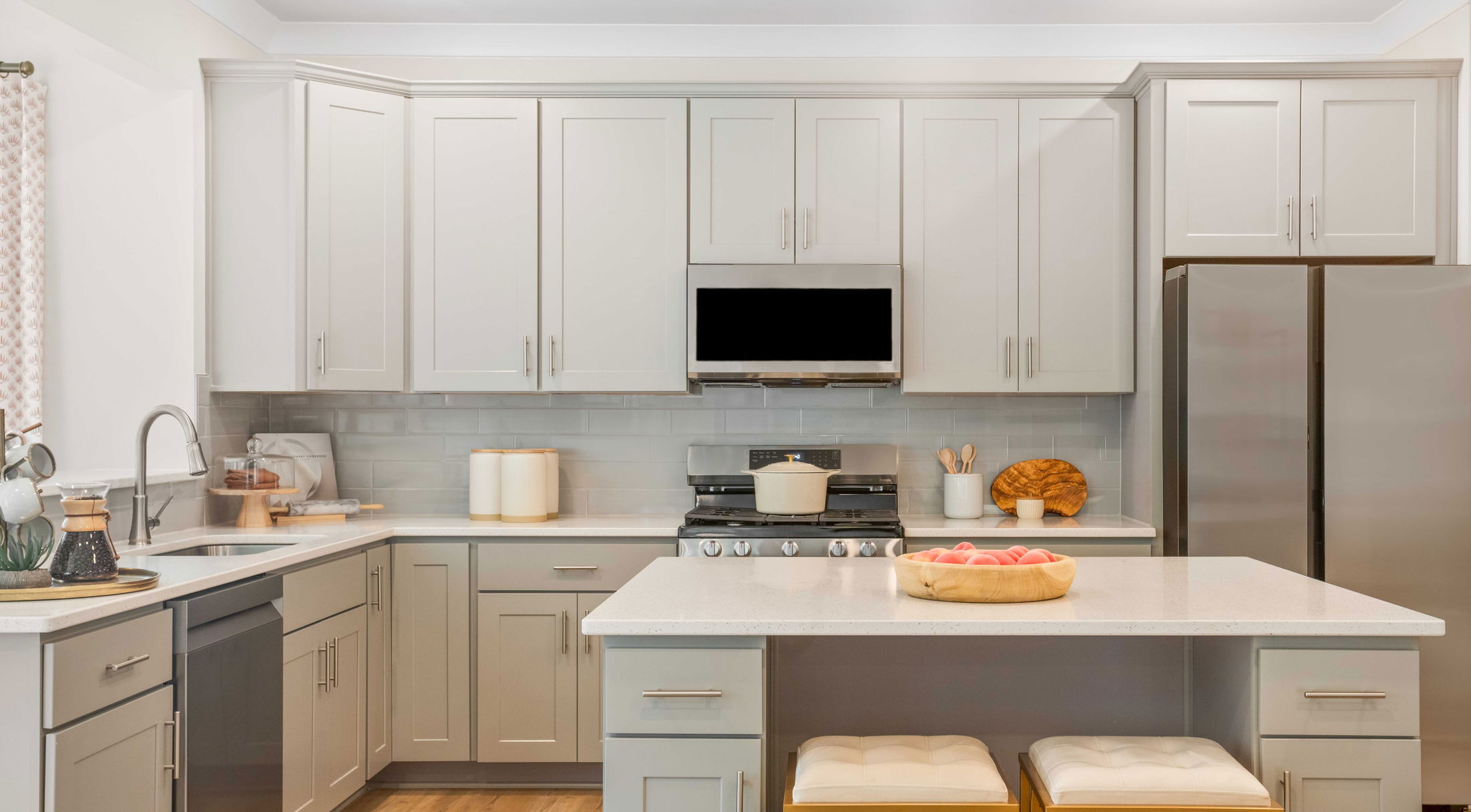 Modern kitchen with light gray cabinets, stainless steel appliances, and a central island with decorative accents.