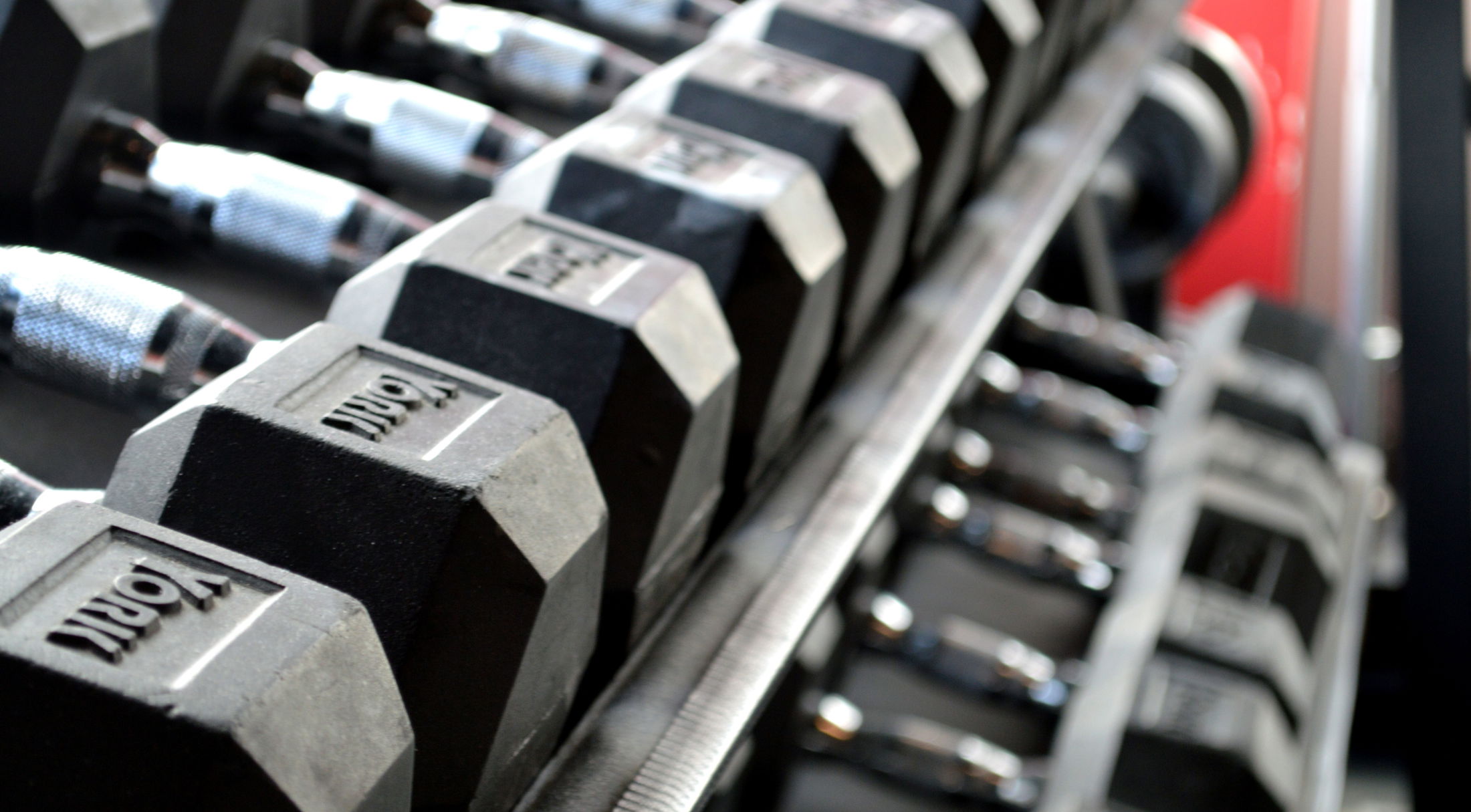 Row of black hexagonal dumbbells neatly arranged on a rack in a gym setting.