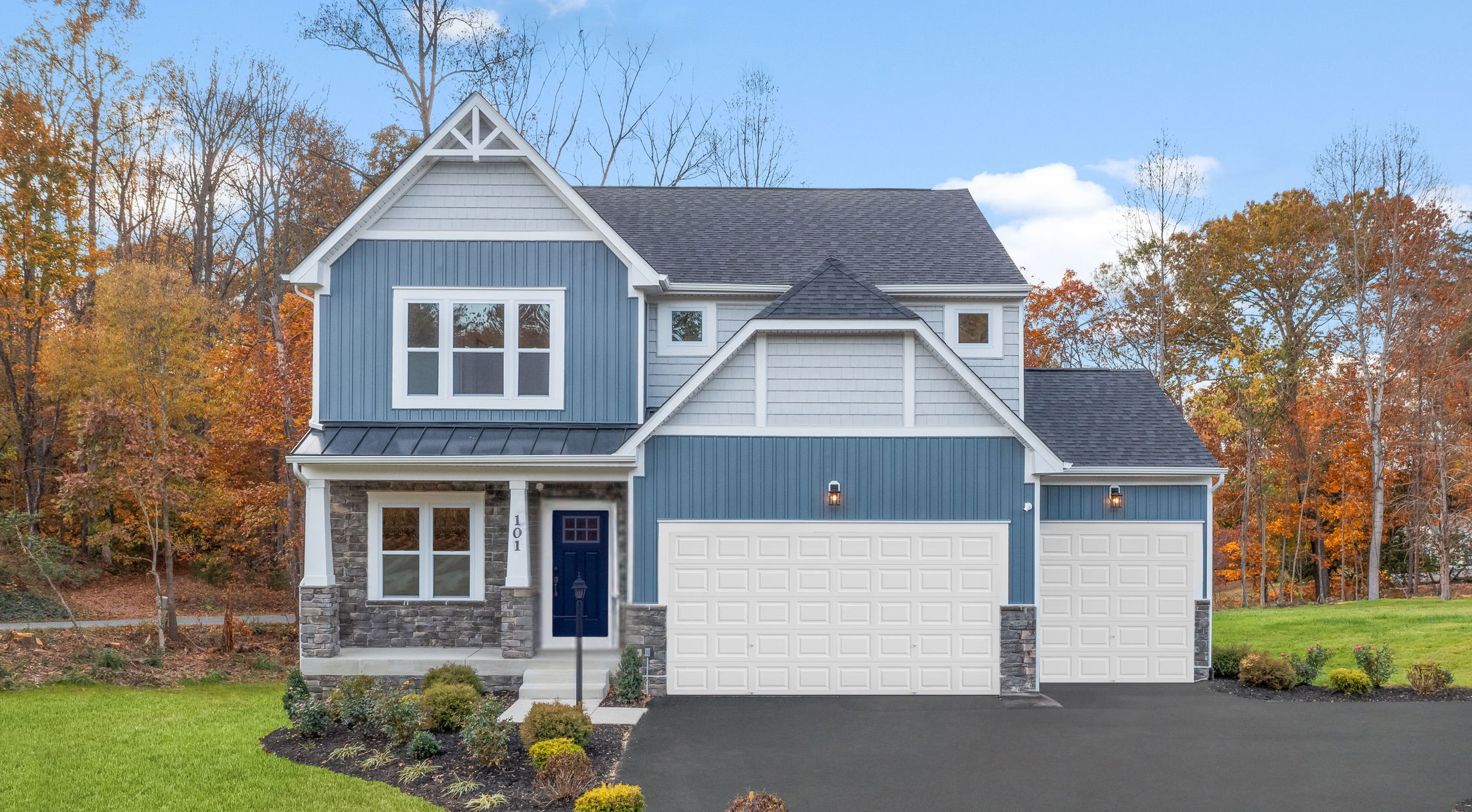 Modern blue and white two-story house with a double garage surrounded by autumn trees.