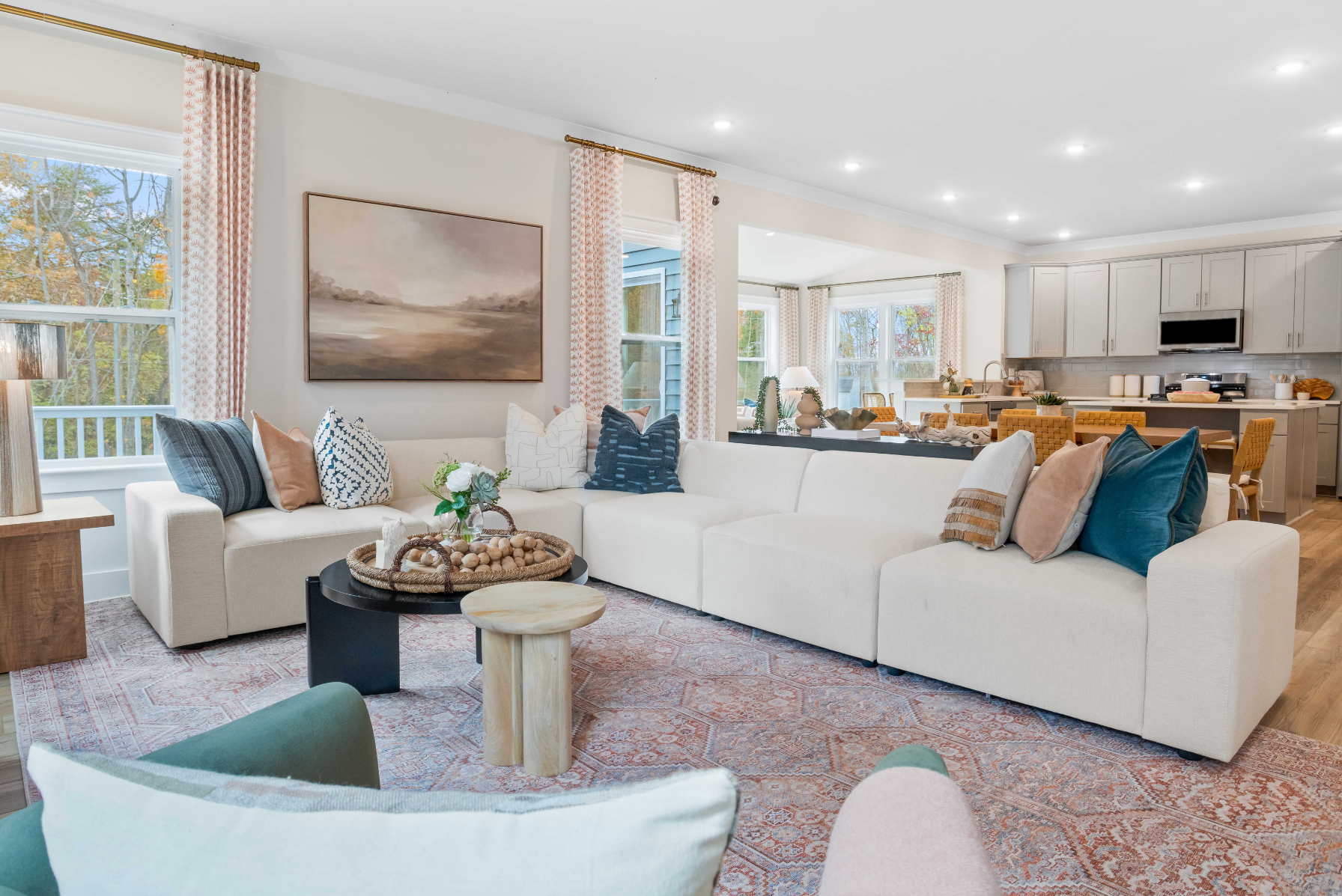 Modern open-concept living room with a cozy white sectional sofa, colorful cushions, stylish décor, and a view into a contemporary kitchen.