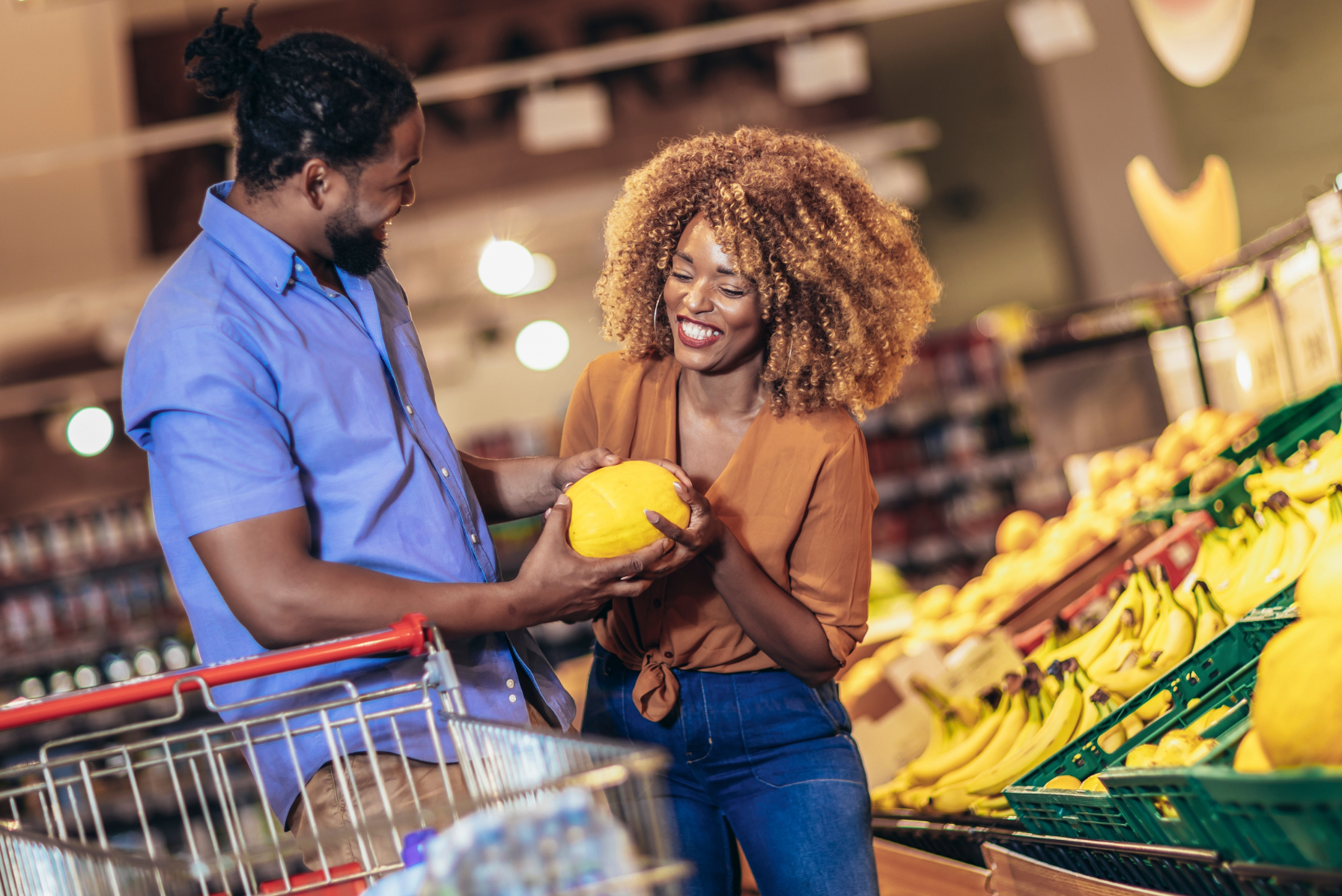 A happy couple shopping for fresh produce and choosing a melon in a grocery store.