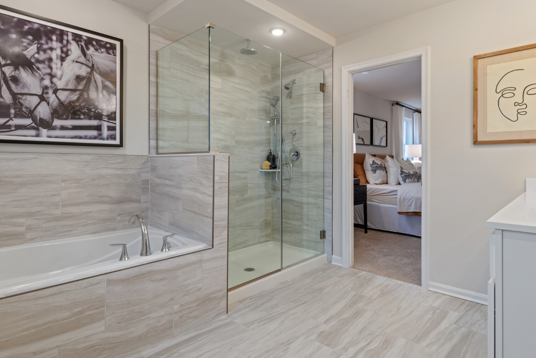 Modern bathroom with glass shower, large bathtub, and view into a stylish bedroom.