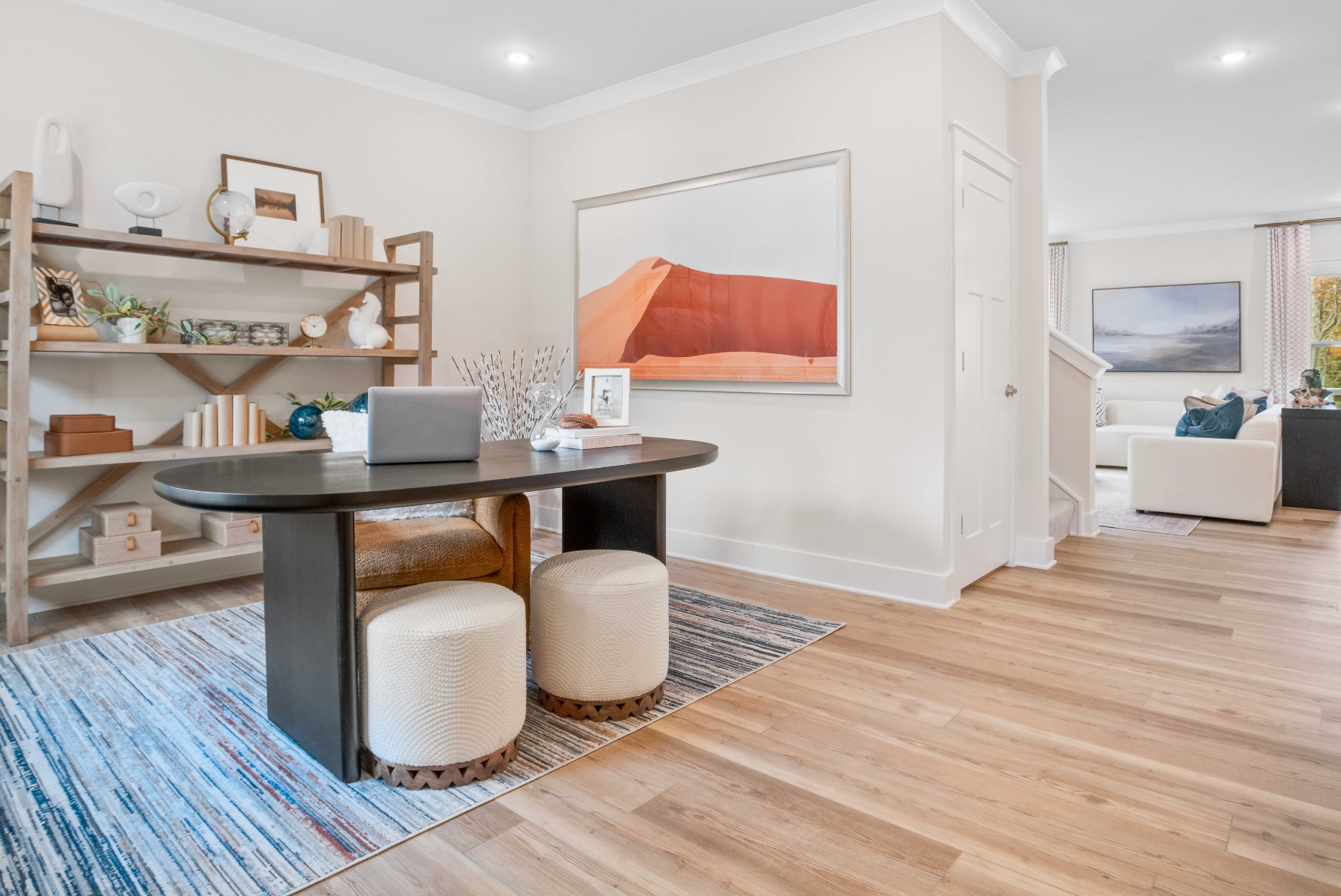 Modern home office with a dark wooden table, cozy pouf seating, and stylish shelving against a light-toned background.