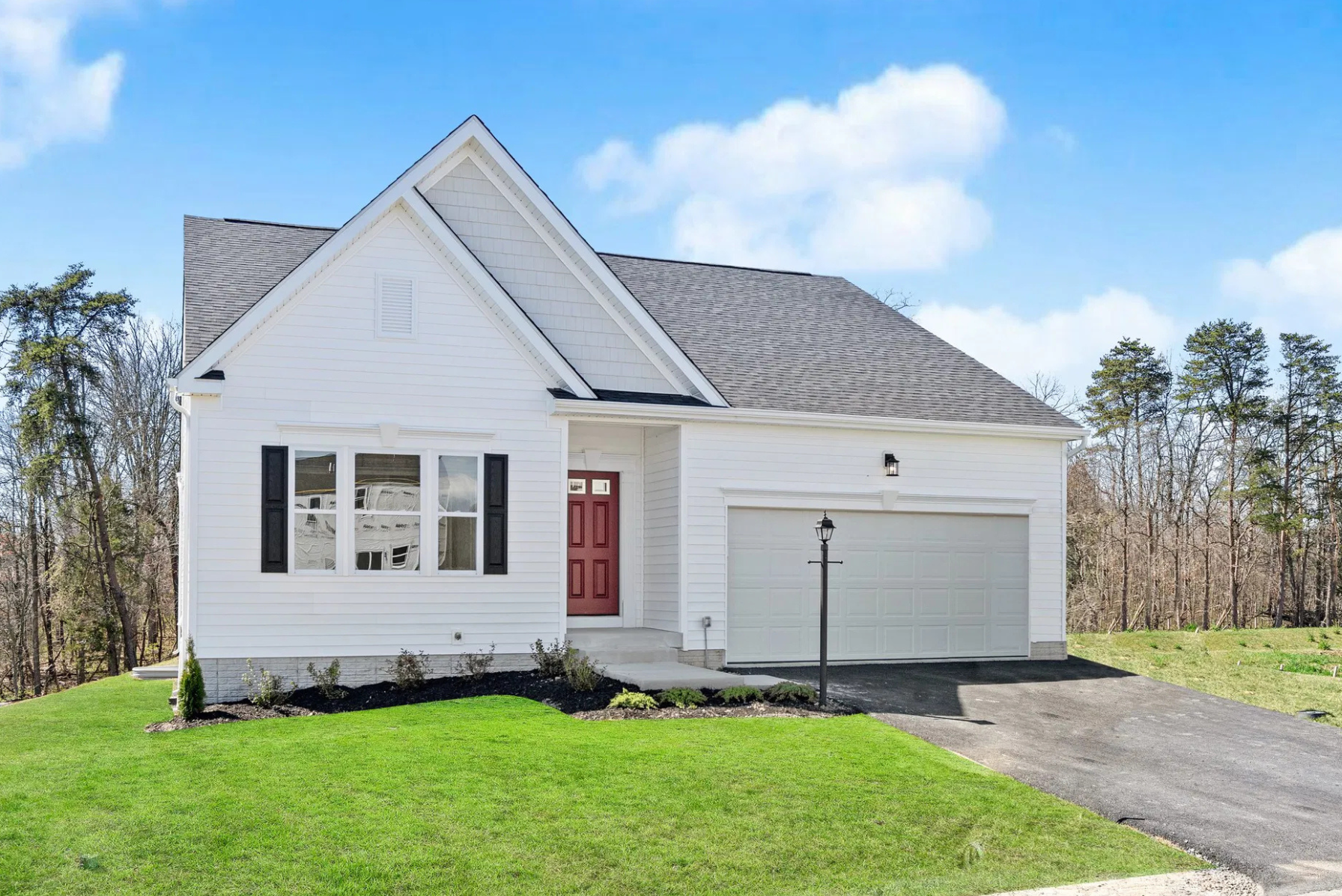 Charming modern single-family home with a red front door, white siding, and attached garage, set against a backdrop of trees and blue sky.