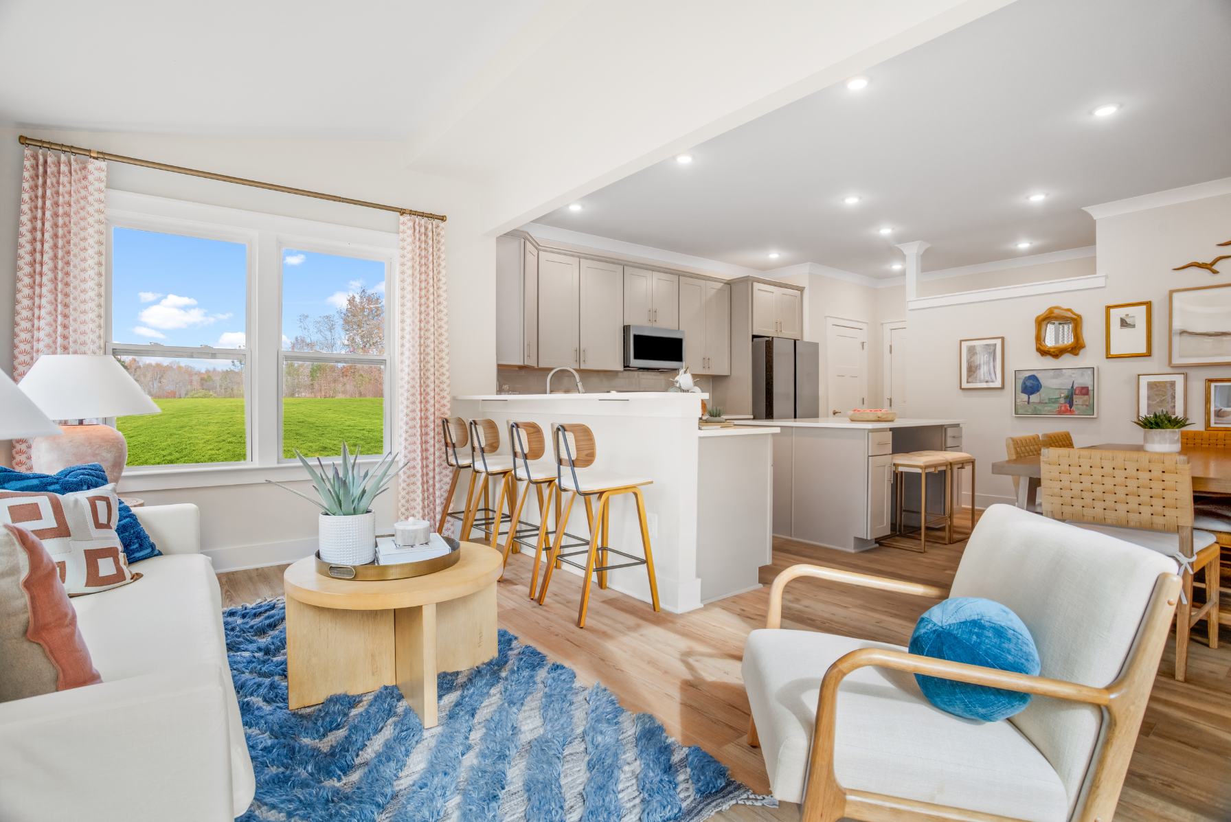 Modern open-concept living room and kitchen with light wood flooring, contemporary furniture, and large windows showcasing a scenic outdoor view.