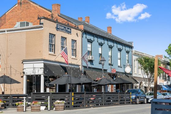 Historic downtown street view featuring charming brick buildings with outdoor dining, festive string lights, and American flags.