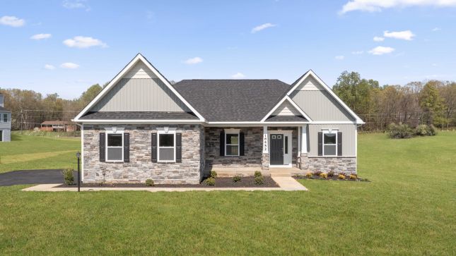 "Modern single-story house with stone exterior and triangular gables set in a spacious green yard."