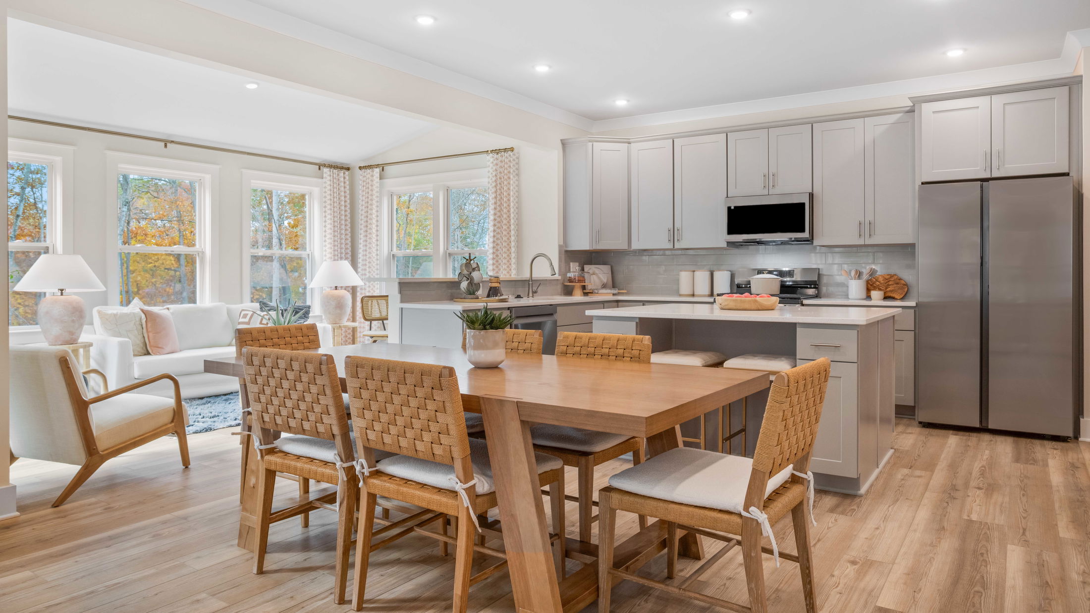 Modern open-concept kitchen and dining area with light wood flooring, featuring woven chairs, a wooden table, and stainless steel appliances.