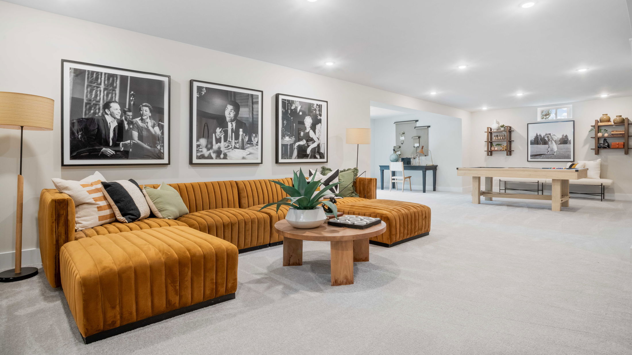 Stylish living room featuring a mustard velvet sectional, wooden coffee table with plant, wall art, and a modern pool table.