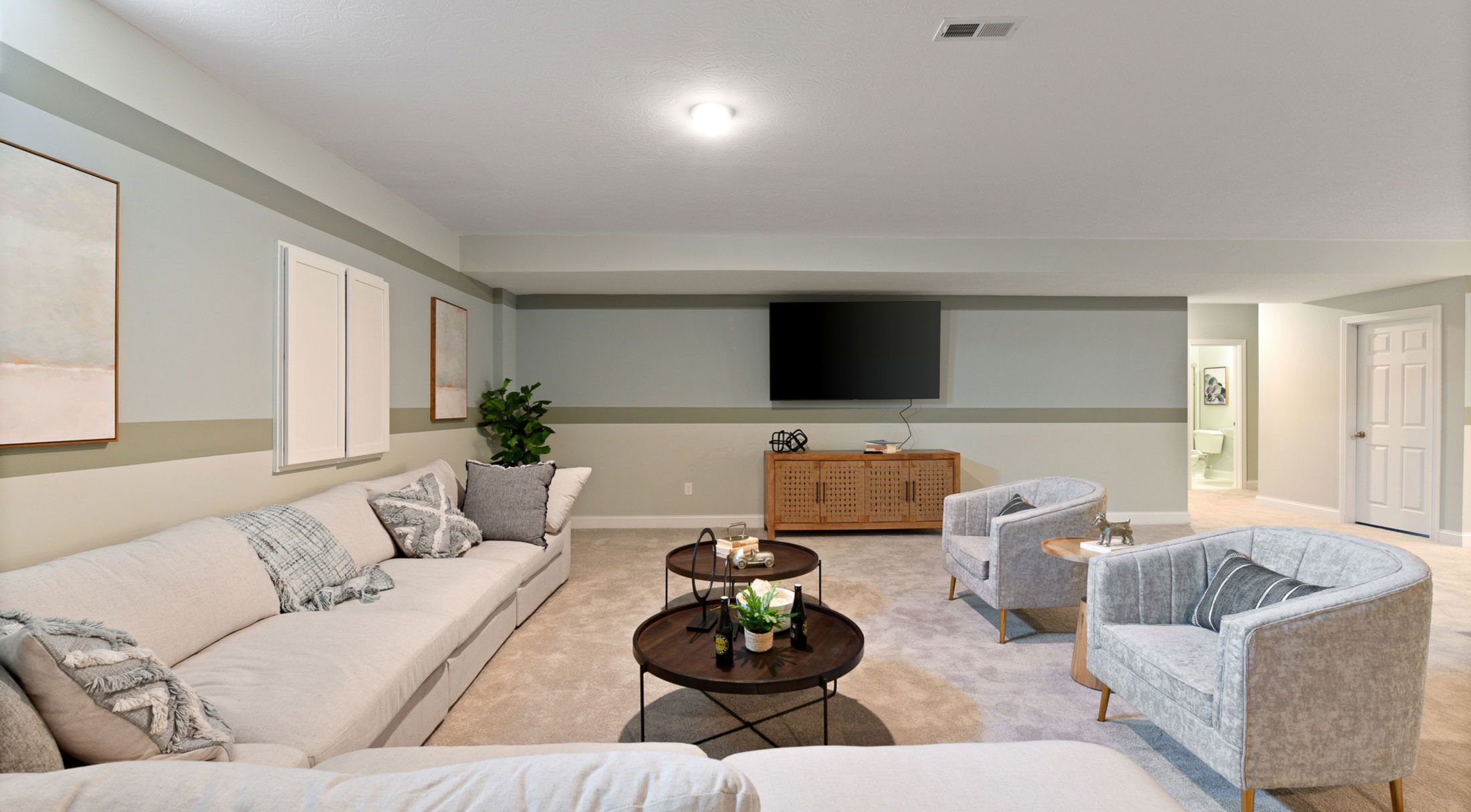 Spacious modern living room with cozy beige sectional, stylish armchairs, round coffee tables, wall-mounted TV, and elegant decor.
