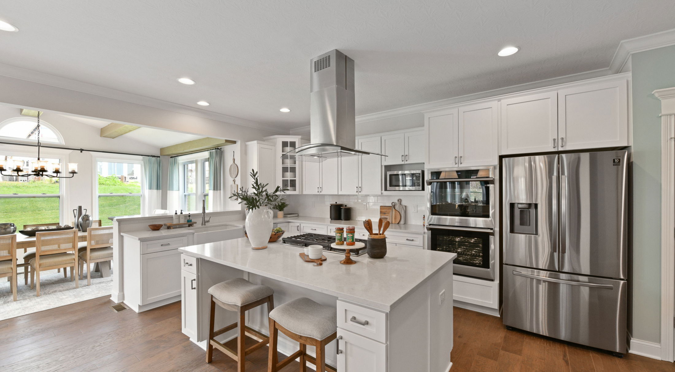 Modern kitchen with white cabinetry, stainless steel appliances, and a central island featuring bar stools and decorative items.