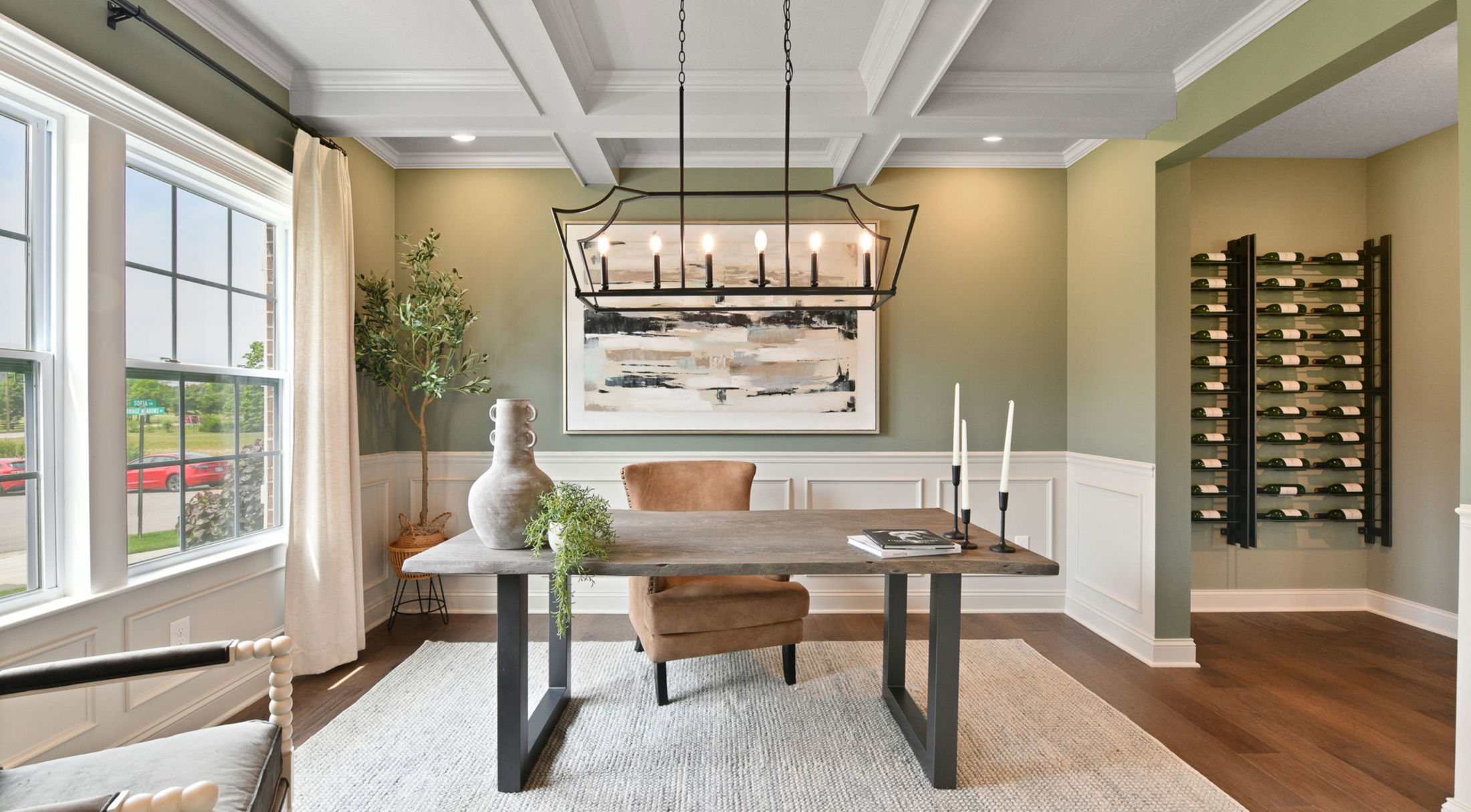 Sophisticated home office with a modern chandelier, contemporary artwork, and a wine rack against sage green walls.