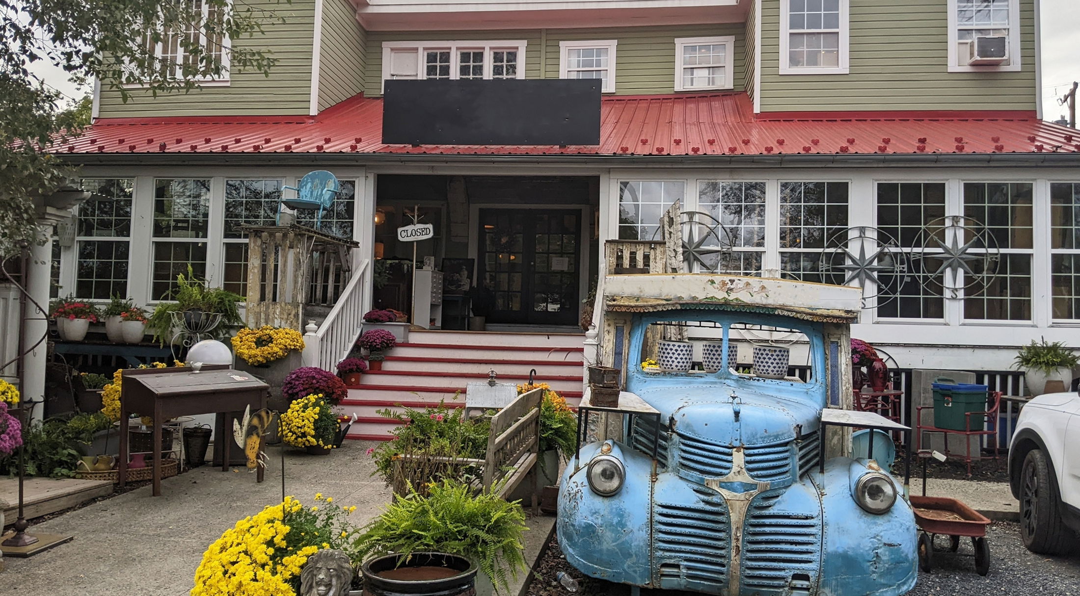 Charming vintage shop entrance with a rustic blue truck, surrounded by vibrant flowers and greenery.