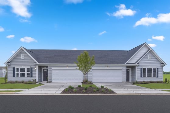 Modern duplex with gray siding and manicured front lawns under a clear blue sky.