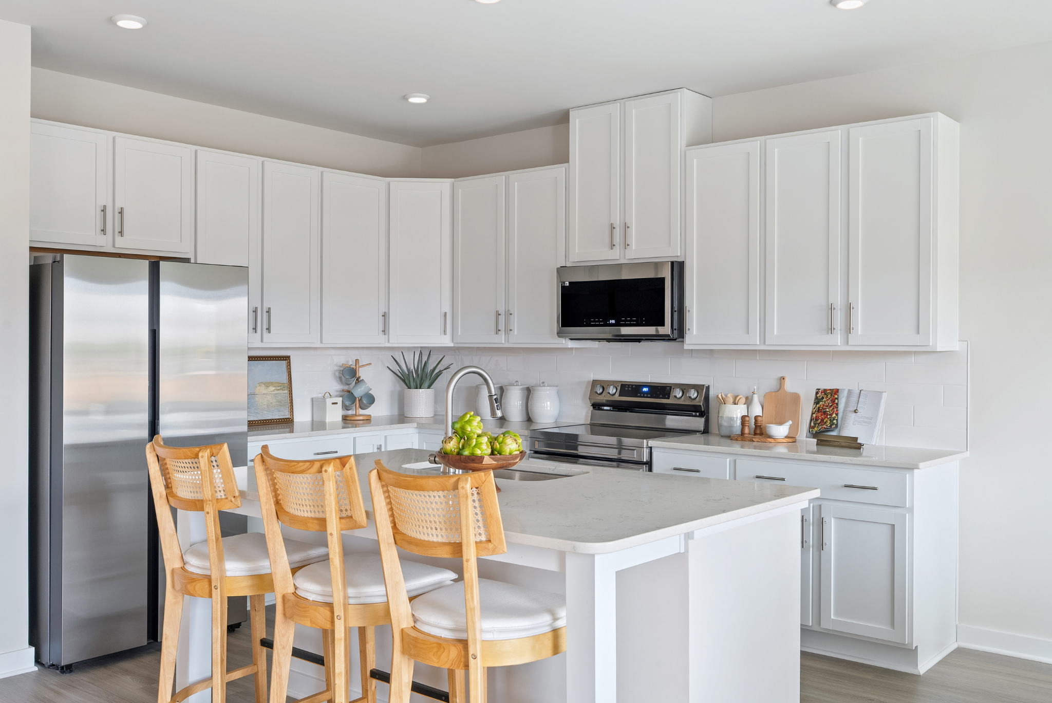 Modern kitchen with white cabinets, stainless steel appliances, and a central island with wooden chairs.