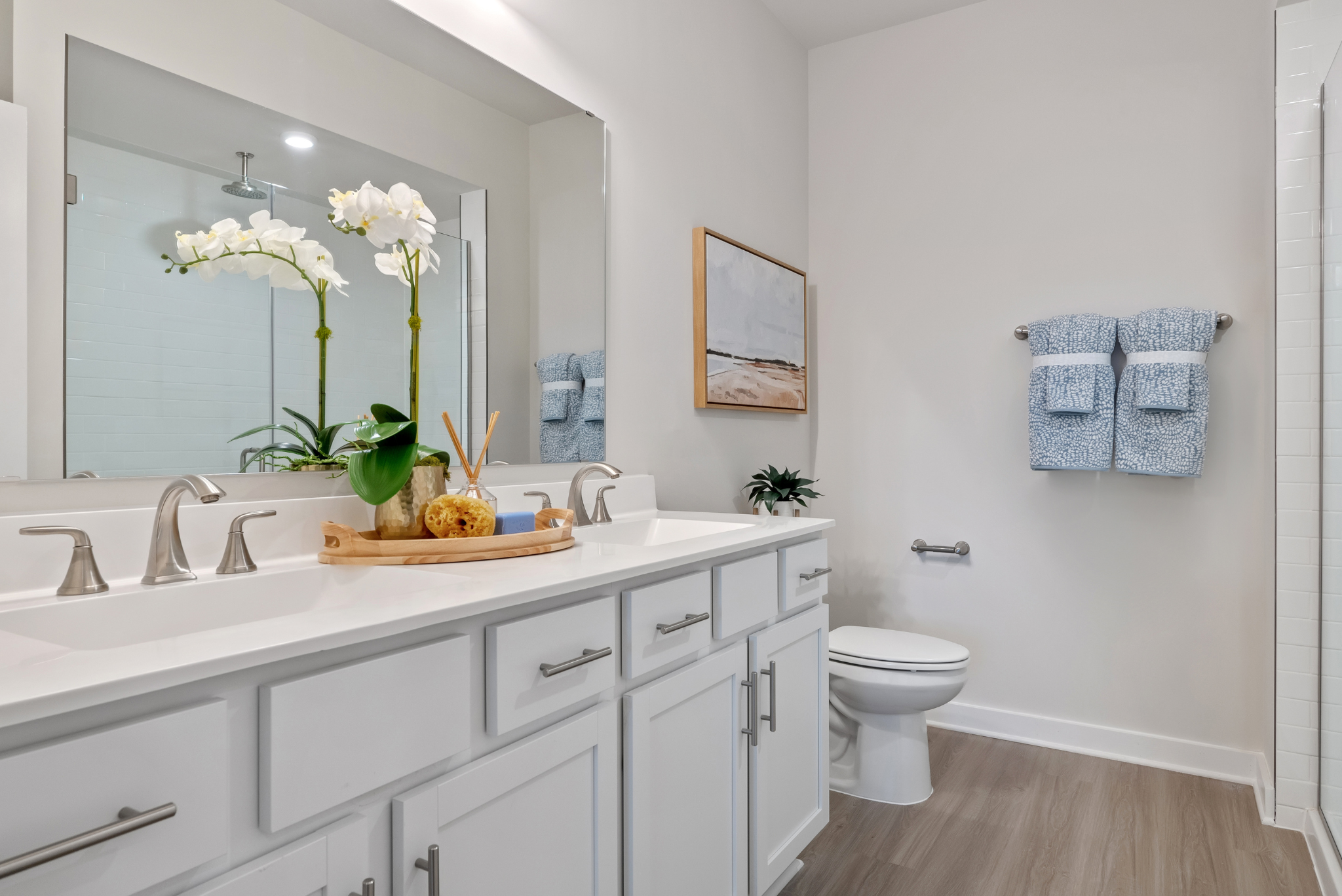 Modern white bathroom with double sink vanity, stylish decor, and blue towels.