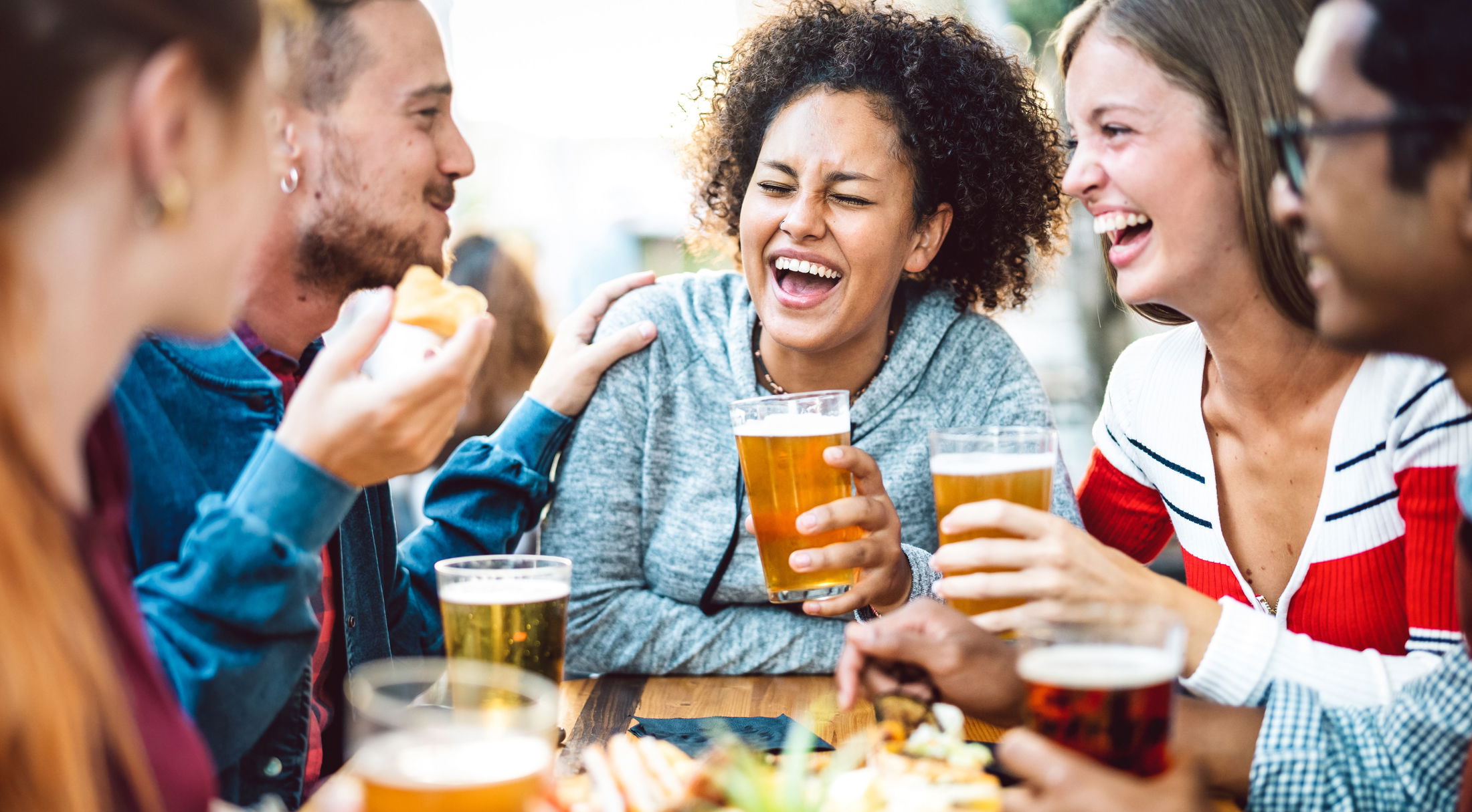 Group of friends laughing and enjoying drinks at an outdoor bar.