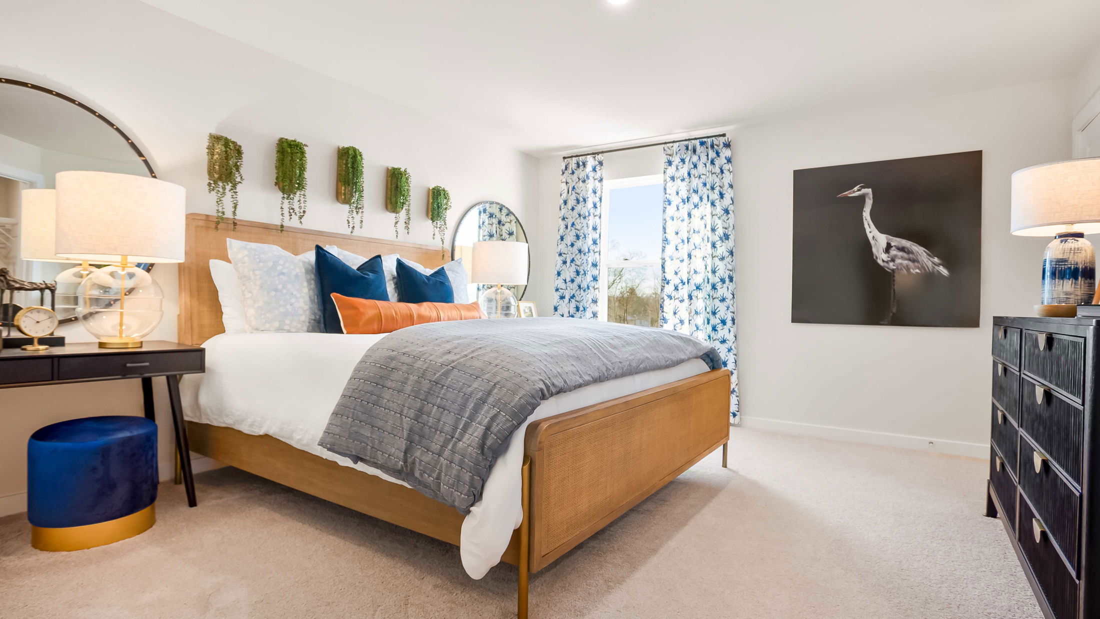 Stylish modern bedroom with a wooden bed, vibrant cushions, floral curtains, and nature-inspired wall decor.