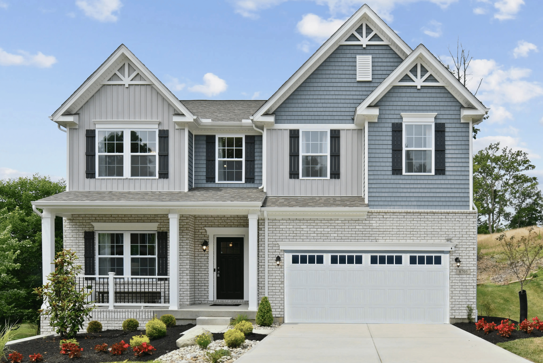 Modern two-story suburban home with gray siding, black shutters, and a landscaped front yard.