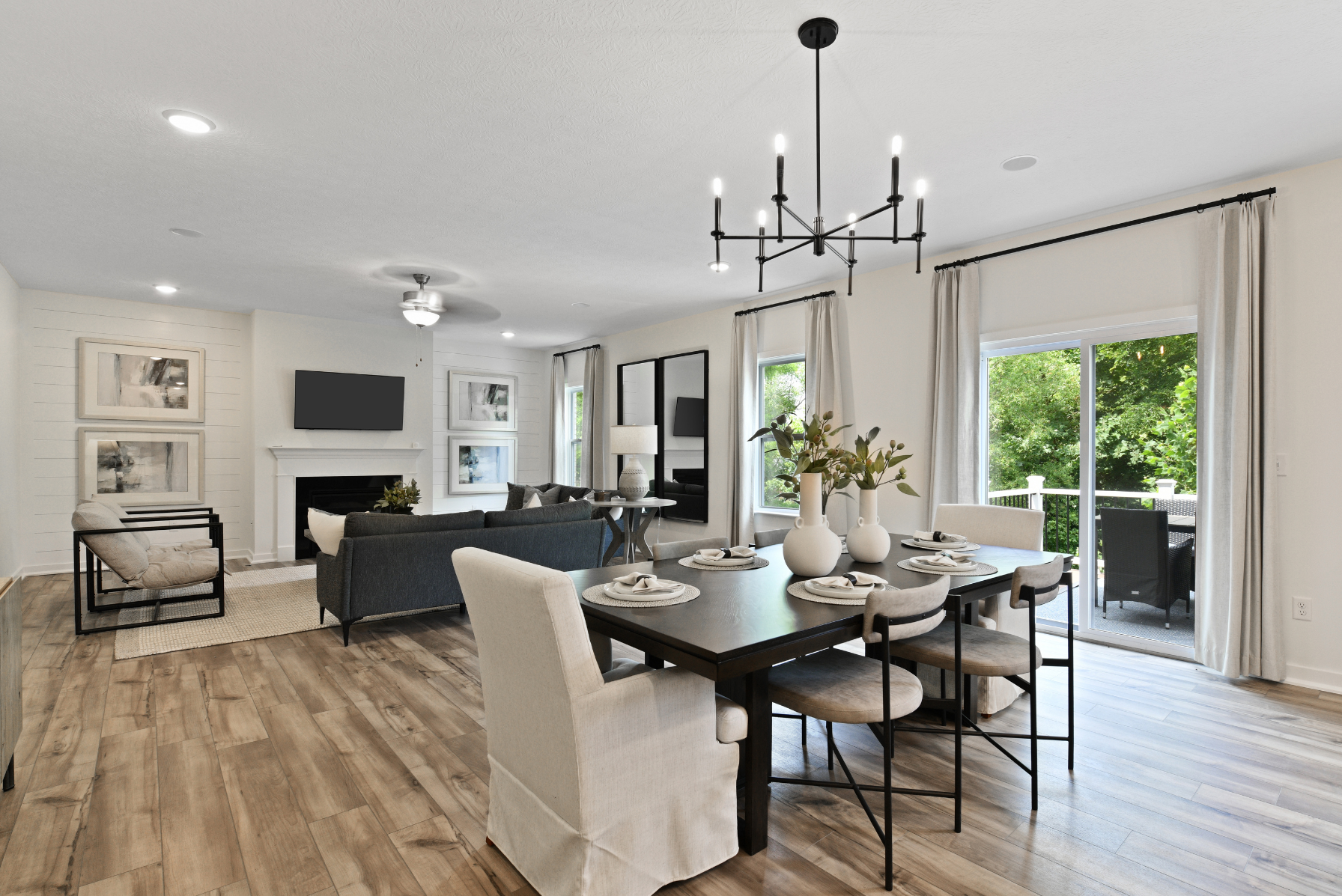 Modern open-plan living room and dining area with hardwood floors, stylish chandelier, and large windows offering natural light and greenery views.