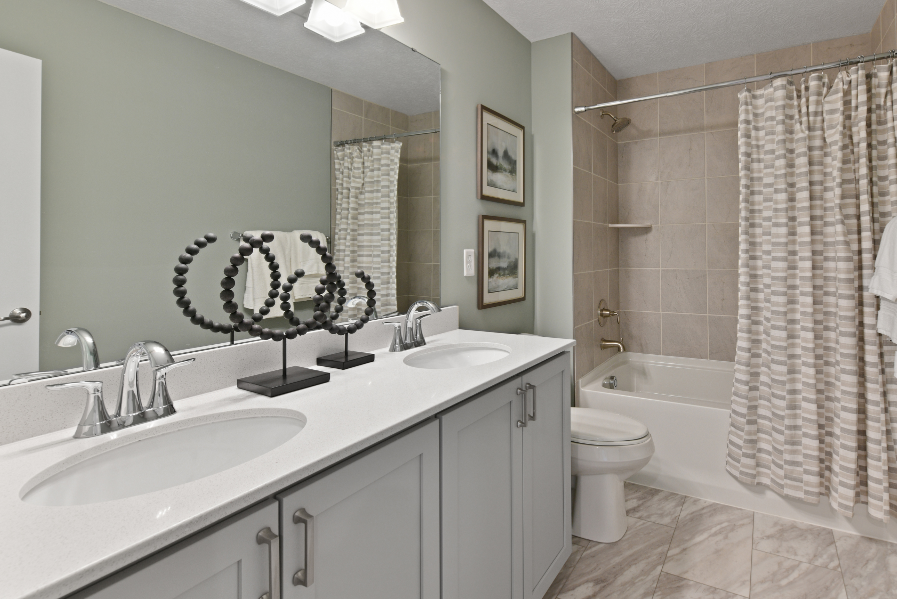 Modern bathroom interior with double vanity, decorative mirror, and bathtub with a beige tile surround.