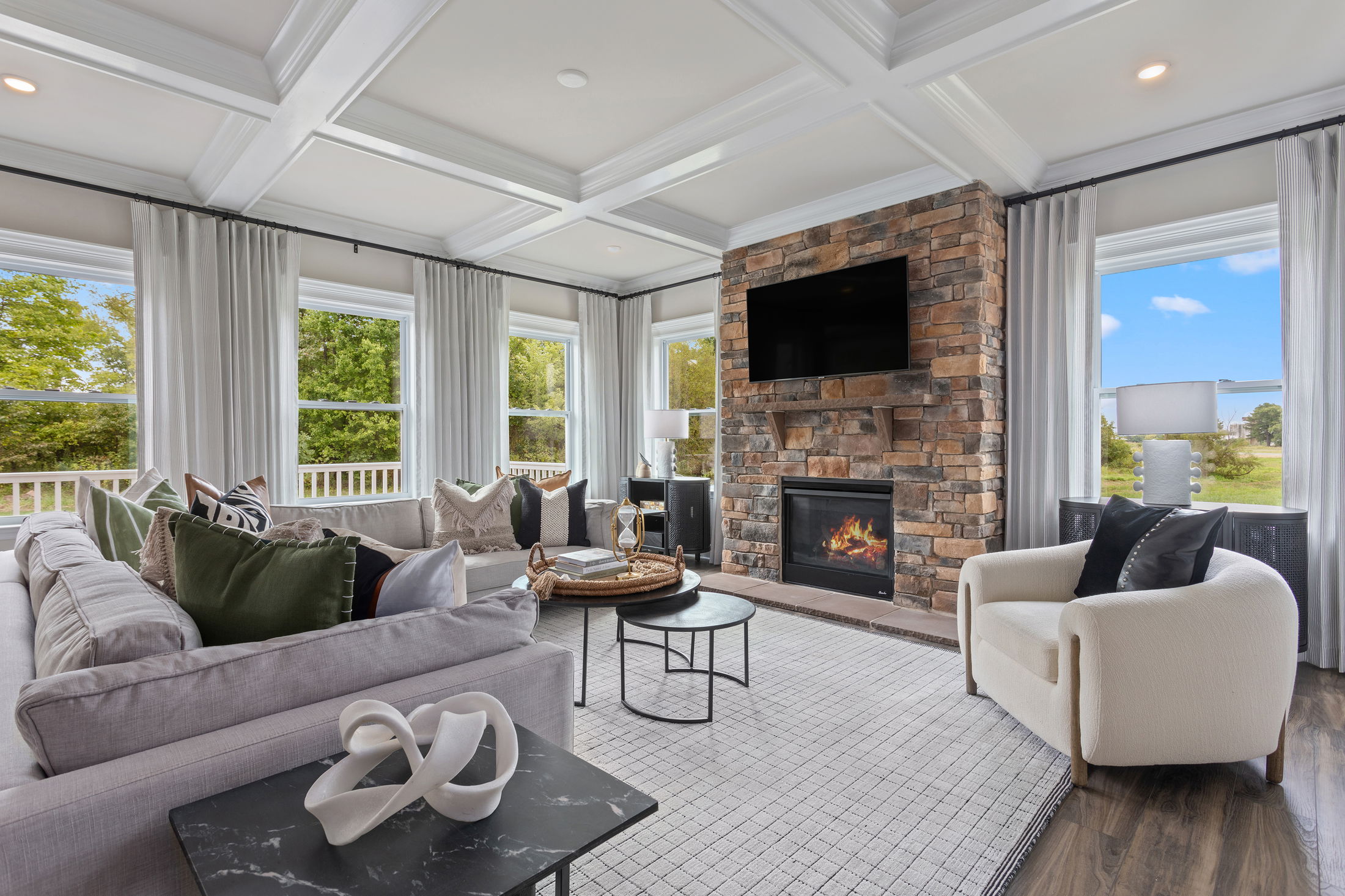 Modern living room with large windows, cozy furniture, stone fireplace, and TV, creating a bright and inviting atmosphere.