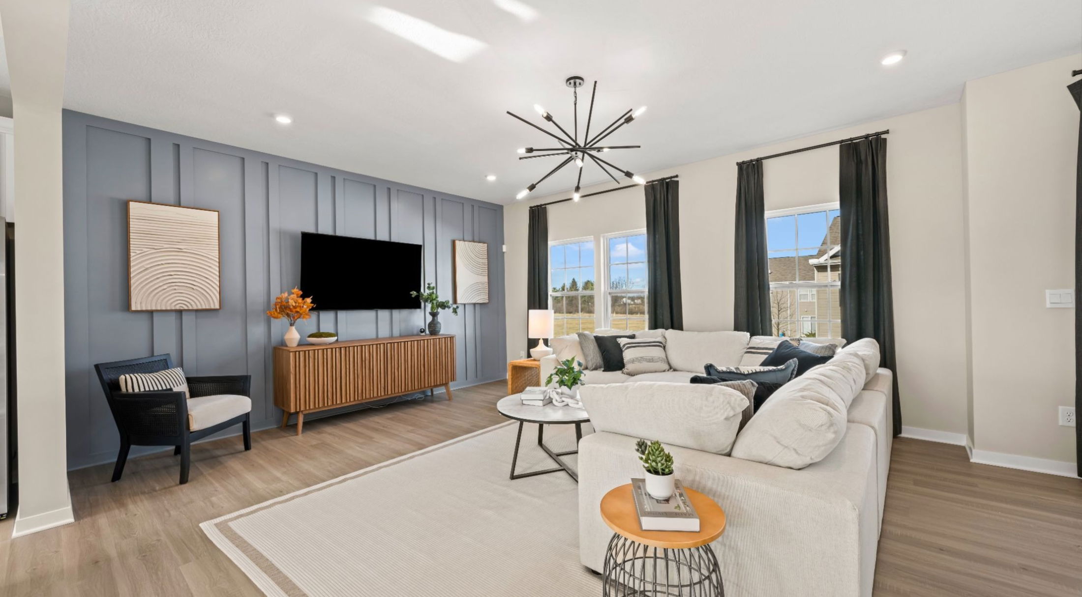 Modern living room interior featuring a beige sectional sofa, stylish lighting fixture, and contemporary decor elements against a blue accent wall.