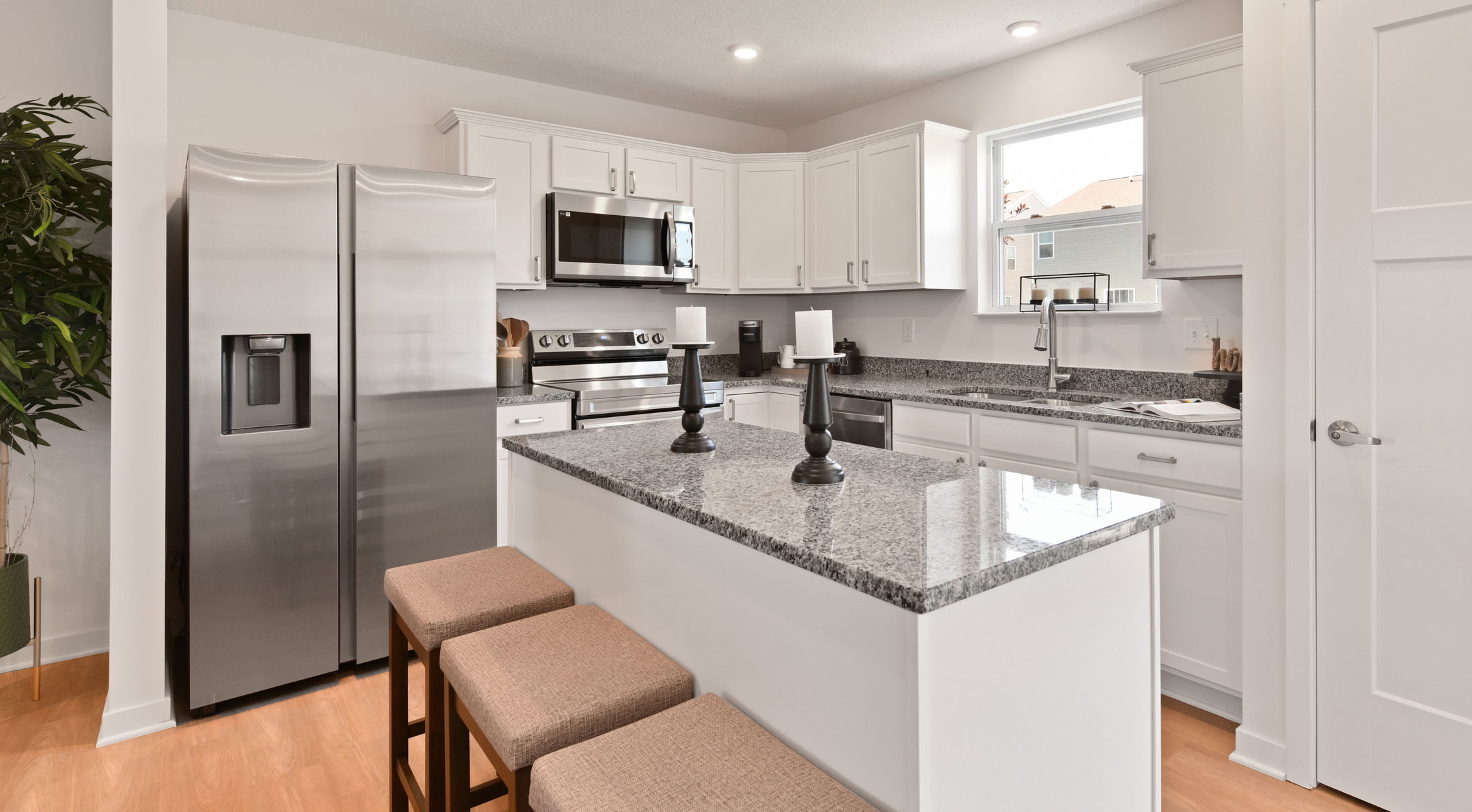 Modern kitchen with white cabinets, stainless steel appliances, and a granite island countertop featuring candle holders.