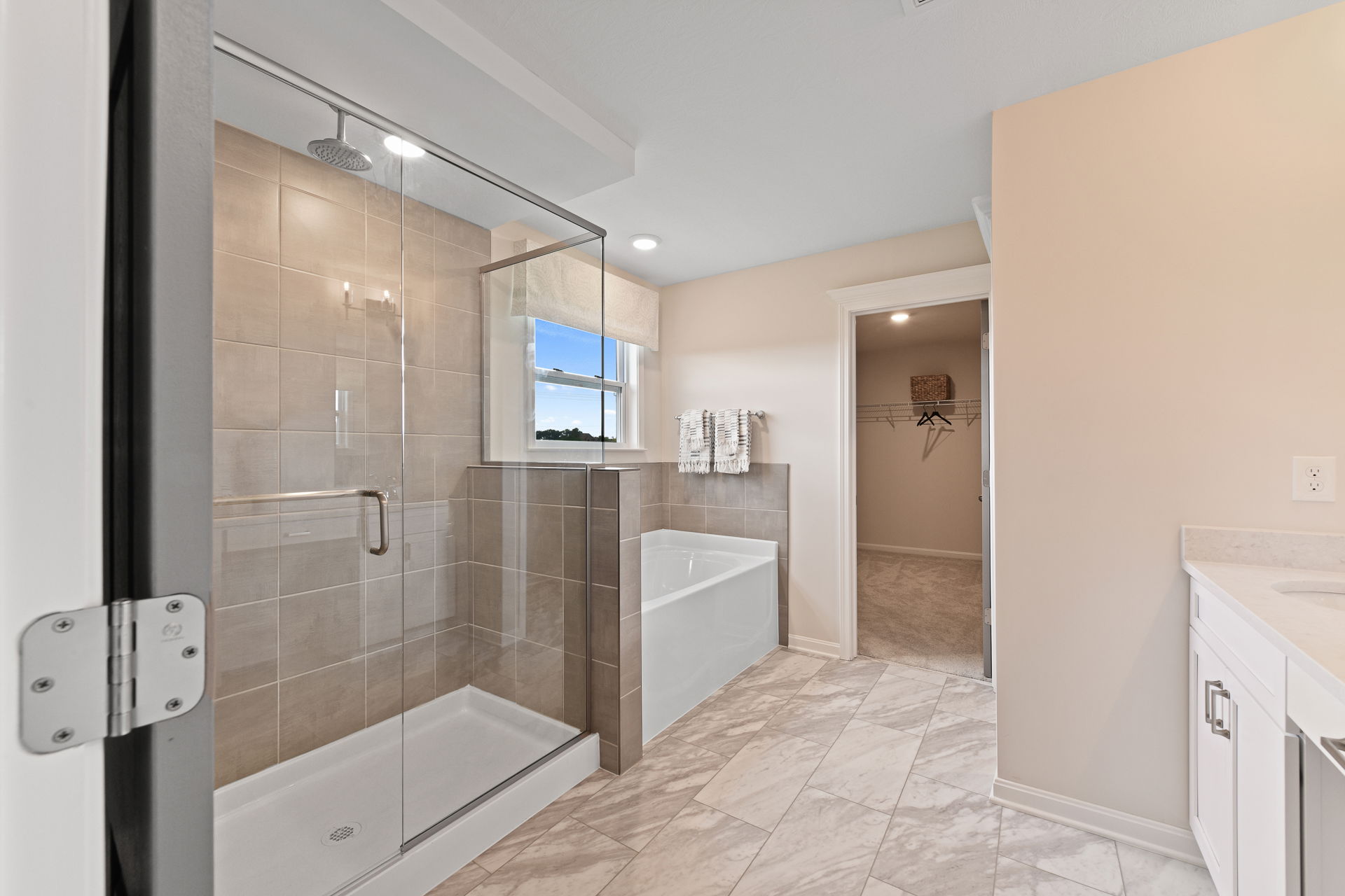 Modern bathroom with glass-enclosed shower, bathtub, and a walk-in closet featuring tiled flooring and a window.