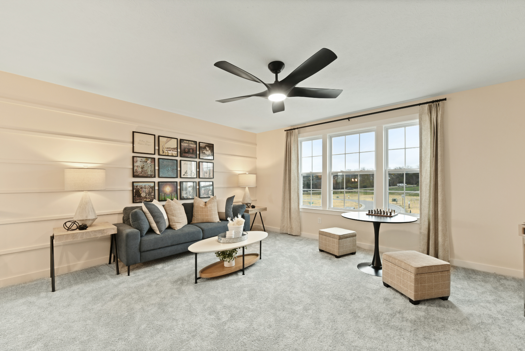 Modern living room with a gray sofa, decorative pillows, wall art, large windows, and a ceiling fan.