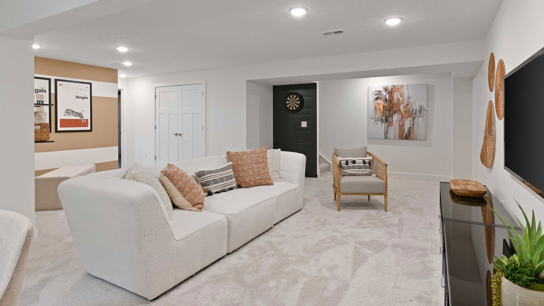 Modern basement living room featuring a cozy white sofa, decorative cushions, wall art, and a dartboard for entertainment.