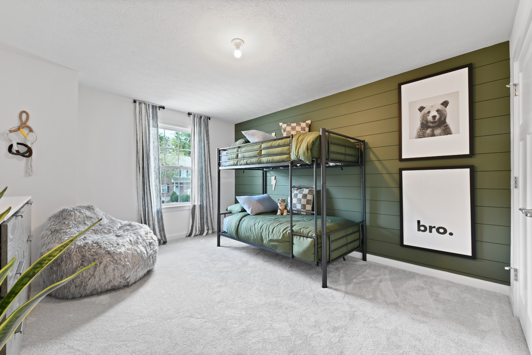 Stylish kids' bedroom featuring green bunk beds, a cozy gray bean bag, and modern wall art on an olive accent wall.