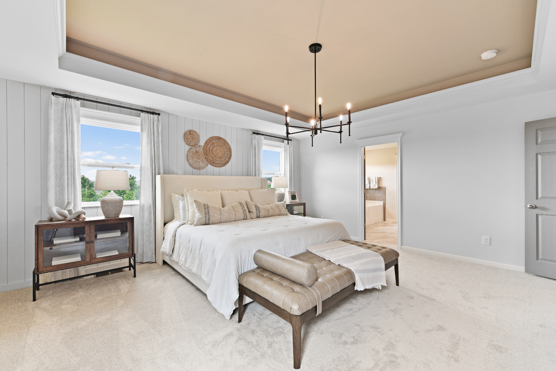 Modern bedroom with white bedding, stylish decor, and a tray ceiling featuring a black chandelier.