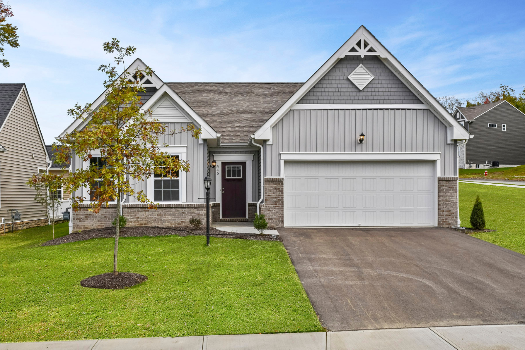 Modern gray suburban home with gabled roof and attached garage, beautifully landscaped front yard.