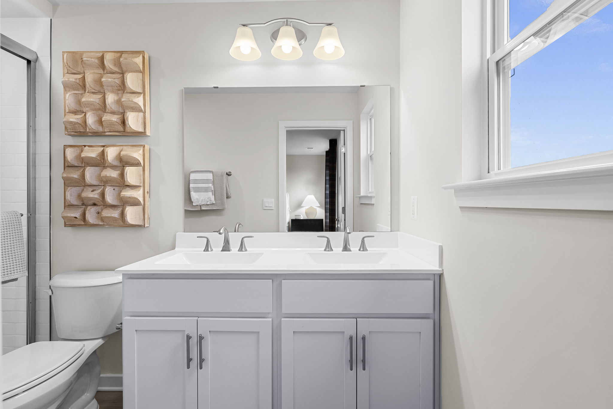 Modern bathroom featuring a double vanity with white cabinets, large mirror, and stylish lighting.