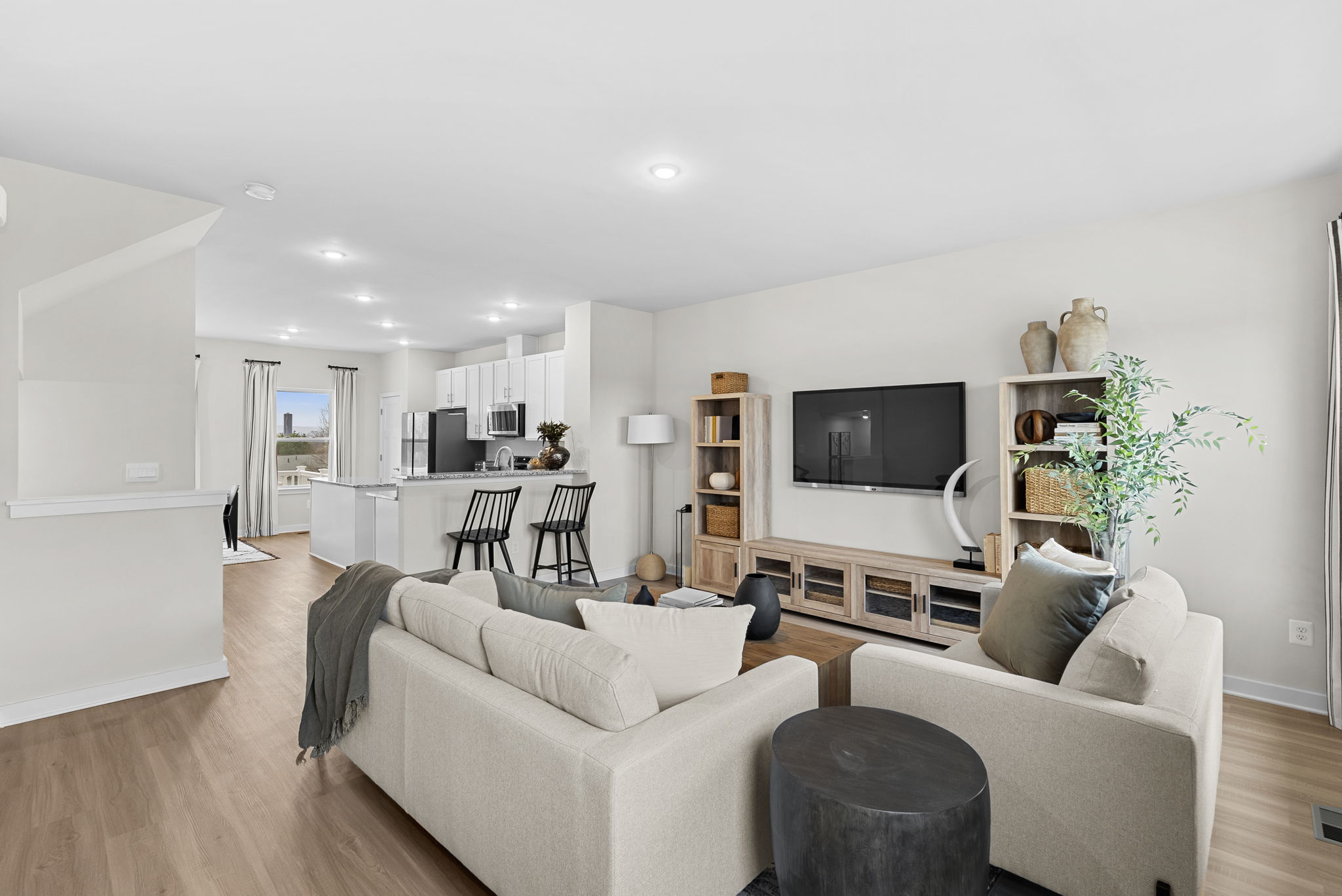Modern open-concept living room and kitchen with stylish neutral decor and a wall-mounted TV.