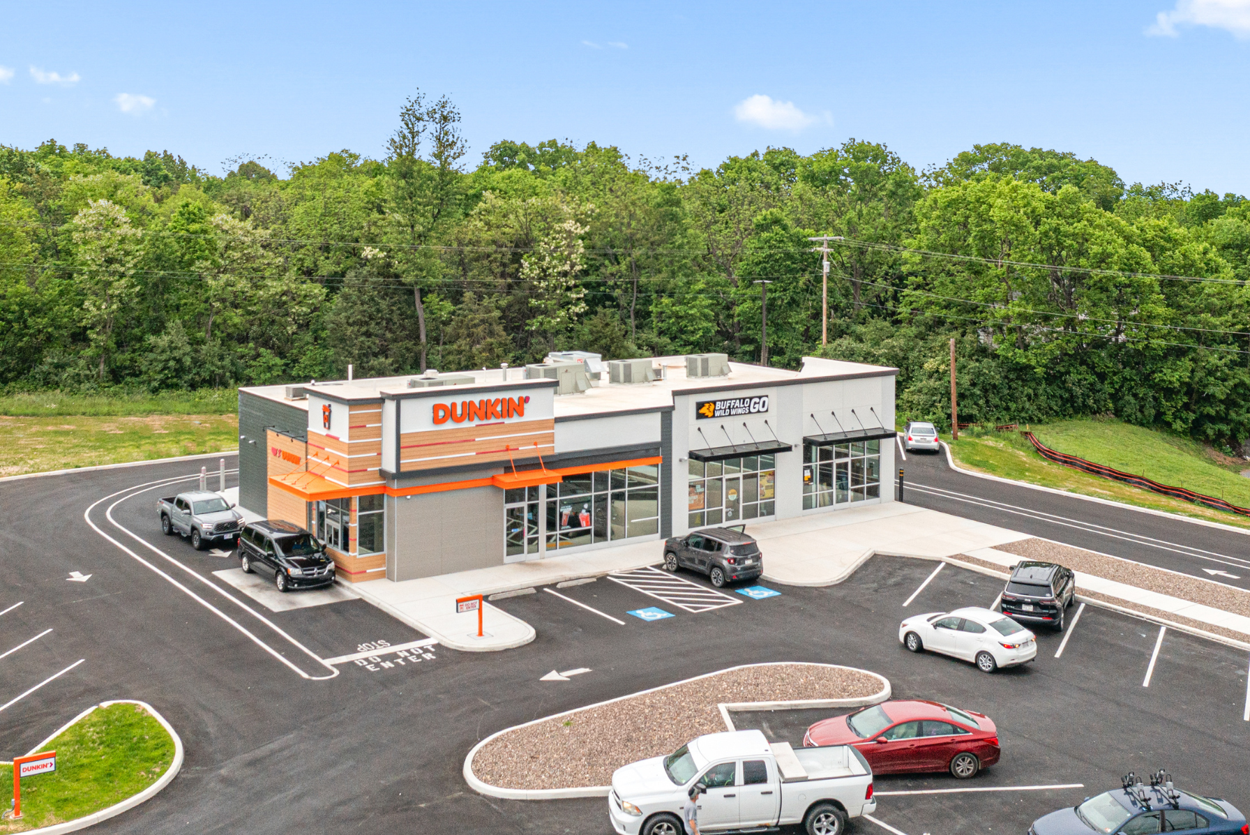 Aerial view of a Dunkin' and Buffalo Wild Wings Go restaurant with surrounding parking lot and green wooded area.