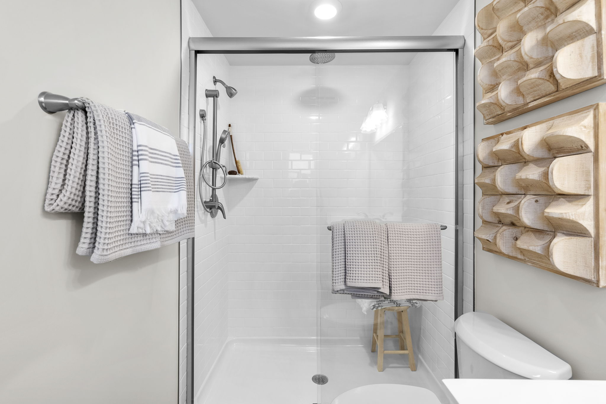 Modern bathroom with glass-enclosed shower, white subway tiles, neatly arranged towels, and wooden wall decor.