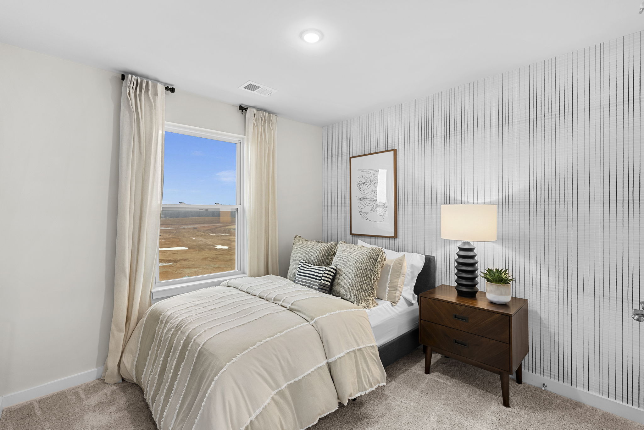 Modern bedroom with a cozy bed, stylish decorative pillows, a bedside lamp, and a scenic outdoor view through the window.