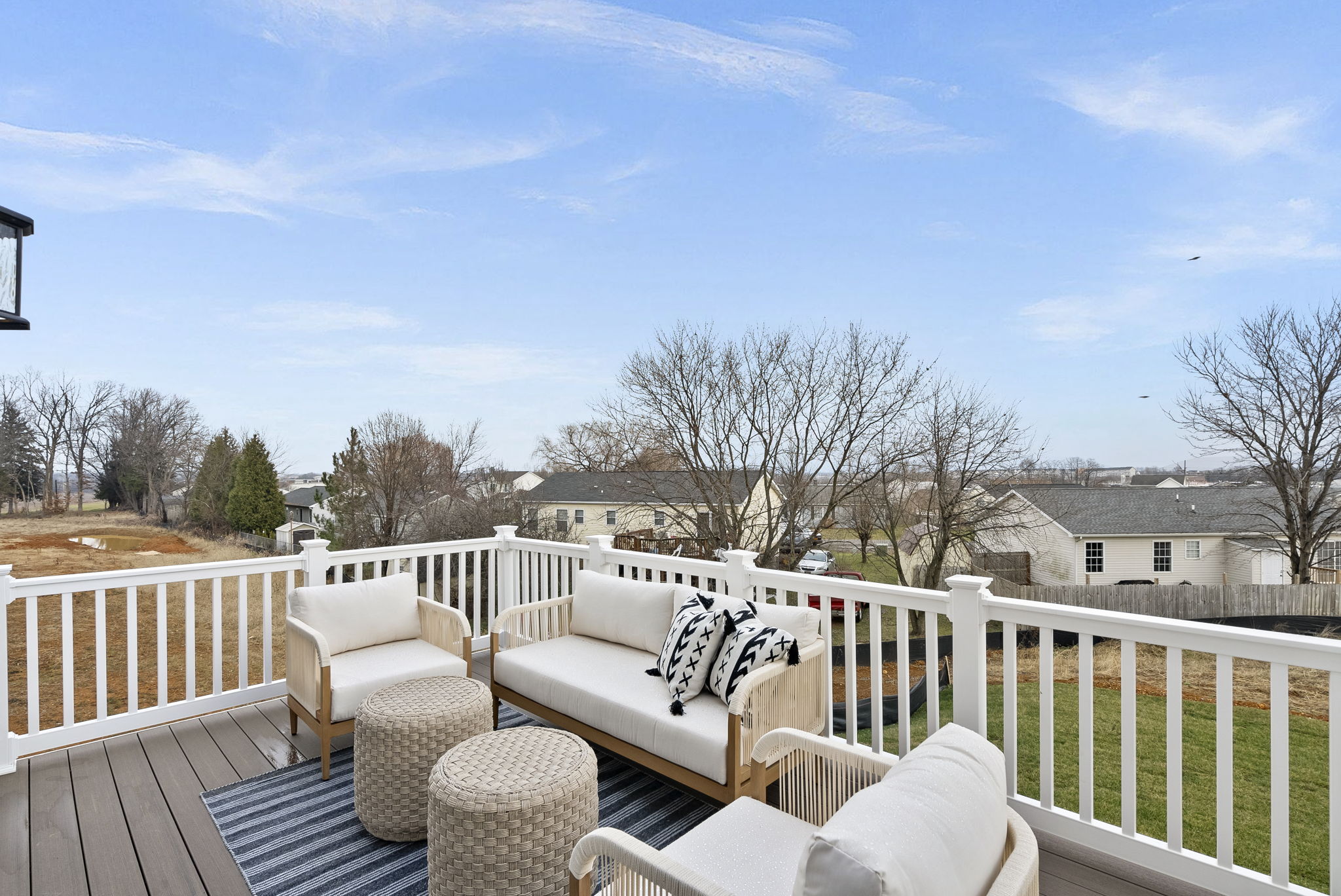 Modern patio with white outdoor furniture on a deck overlooking a suburban neighborhood and trees under a clear blue sky.