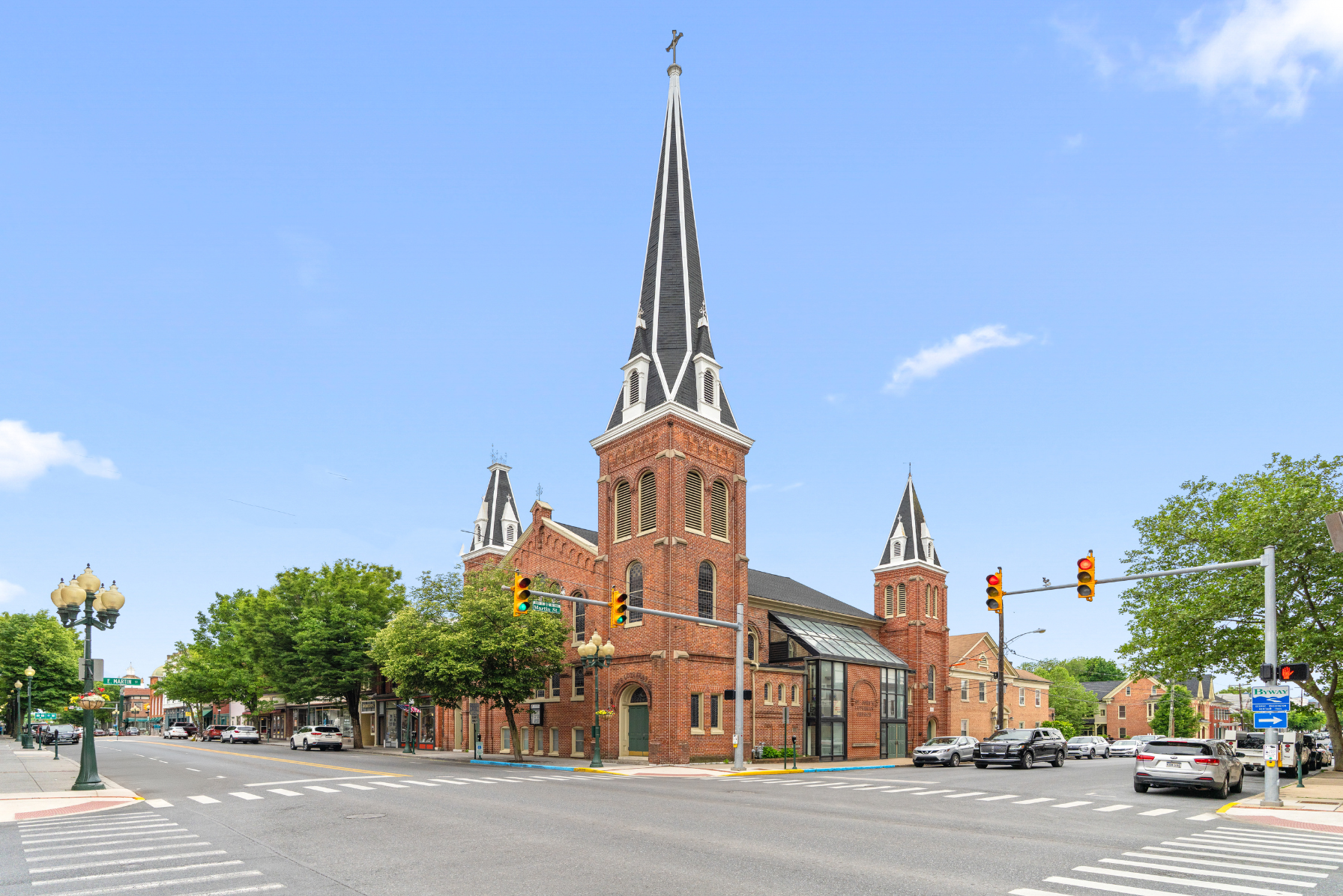 Historic brick church with tall spires on a bustling street corner in a small-town setting.